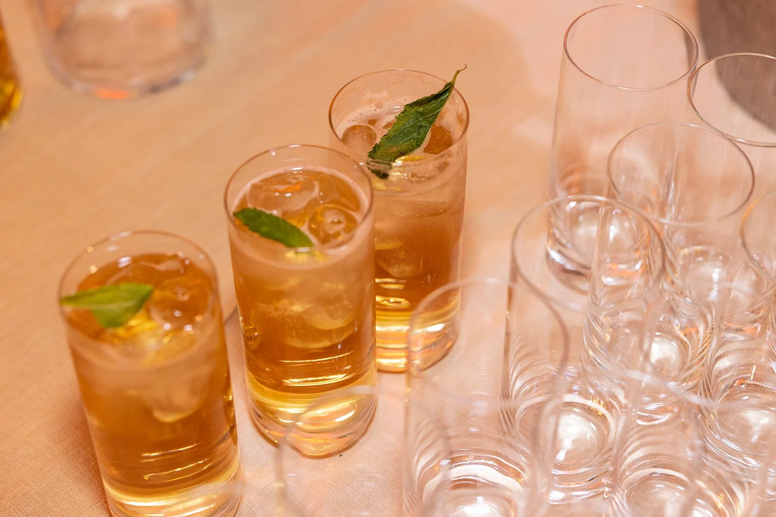Three glasses of iced tea with mint leaves on a table with several empty glasses.