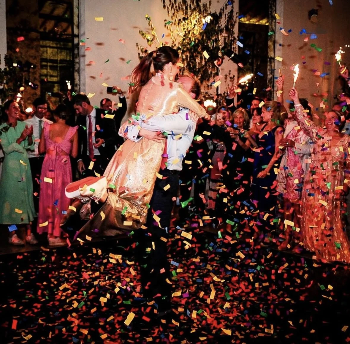 People celebrating with confetti, dancing, and hugging at a lively party or wedding reception.