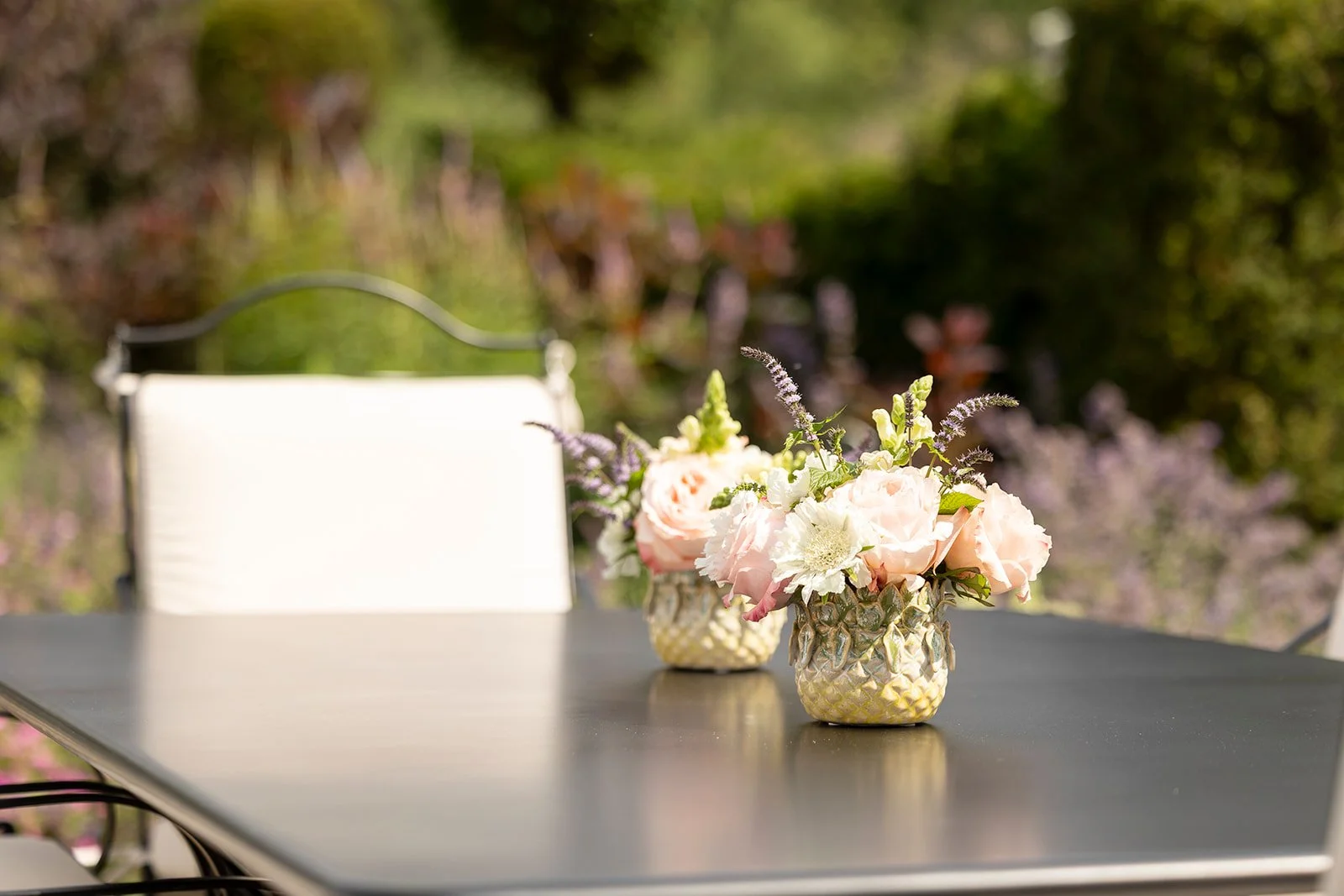 Two vases with pink and white flowers on a black outdoor table, with a blurred natural green background.