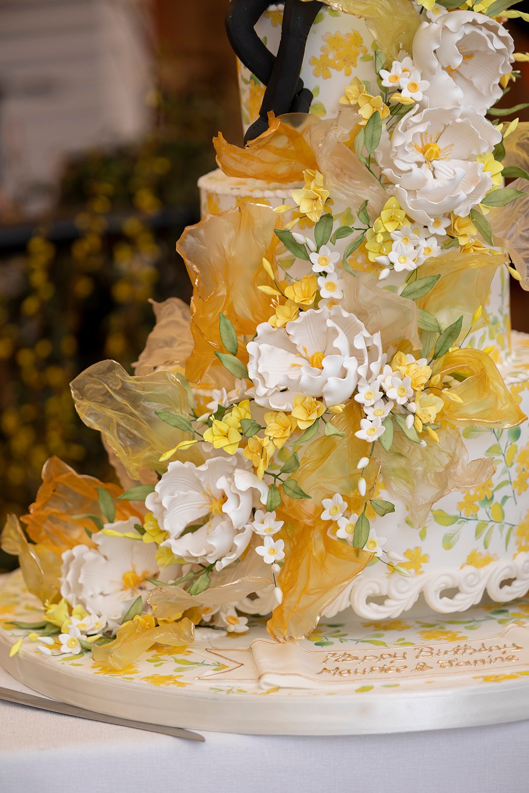 A decorated birthday cake with white, yellow, and green floral and leaf decorations.