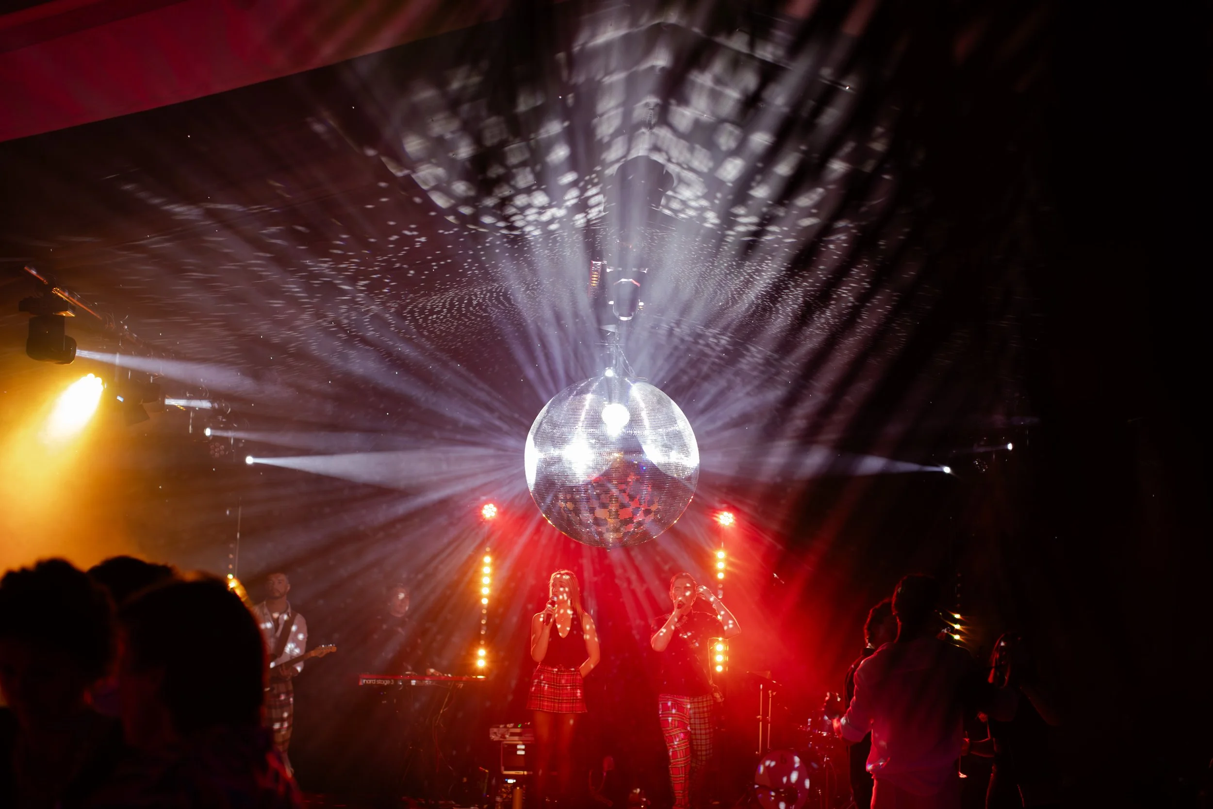 People dancing and singing under a large disco ball with bright lights and laser effects at a concert or nightclub.