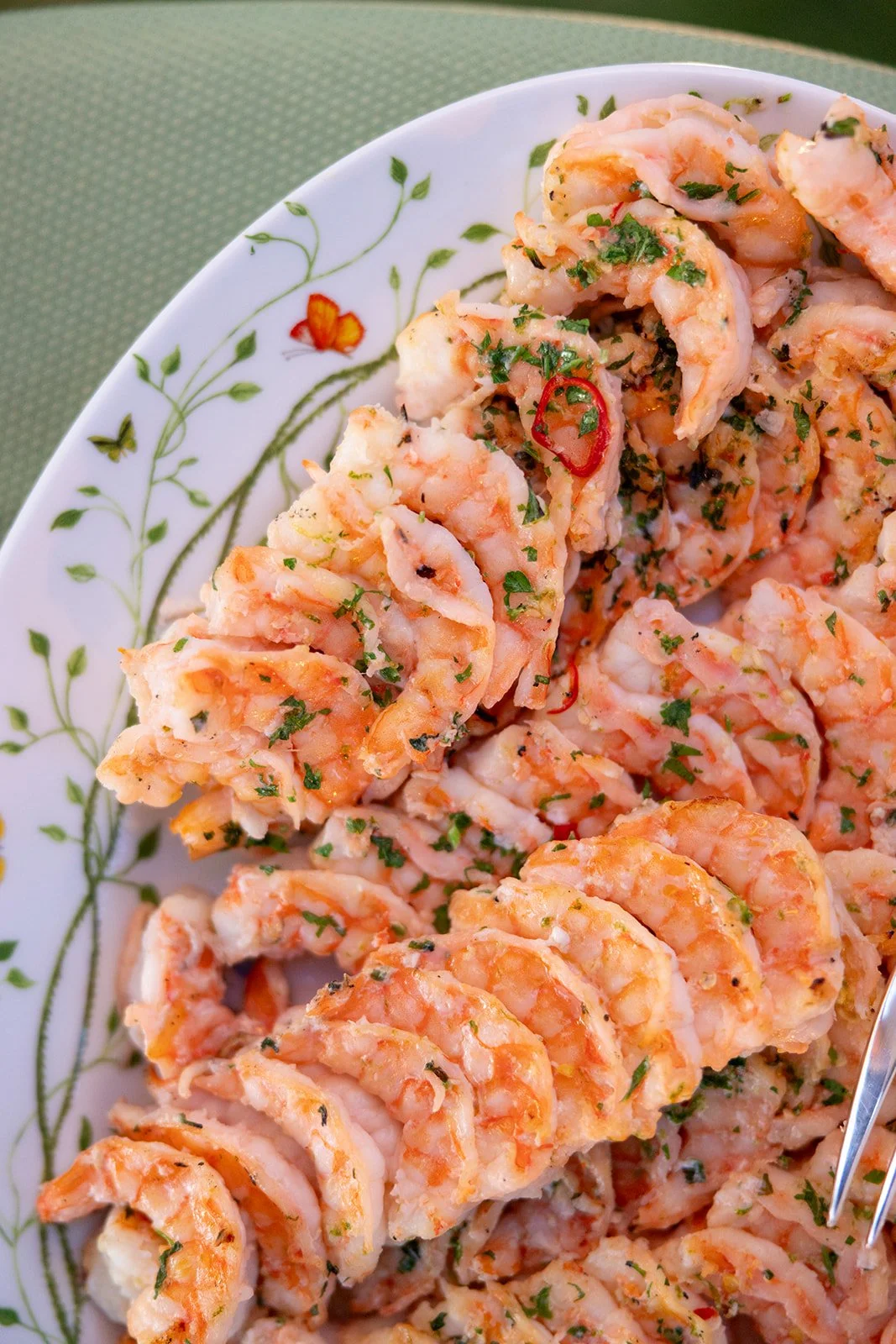 Plate of cooked, chopped seafood garnished with herbs, with visible slices of red chili pepper, on a decorative plate.