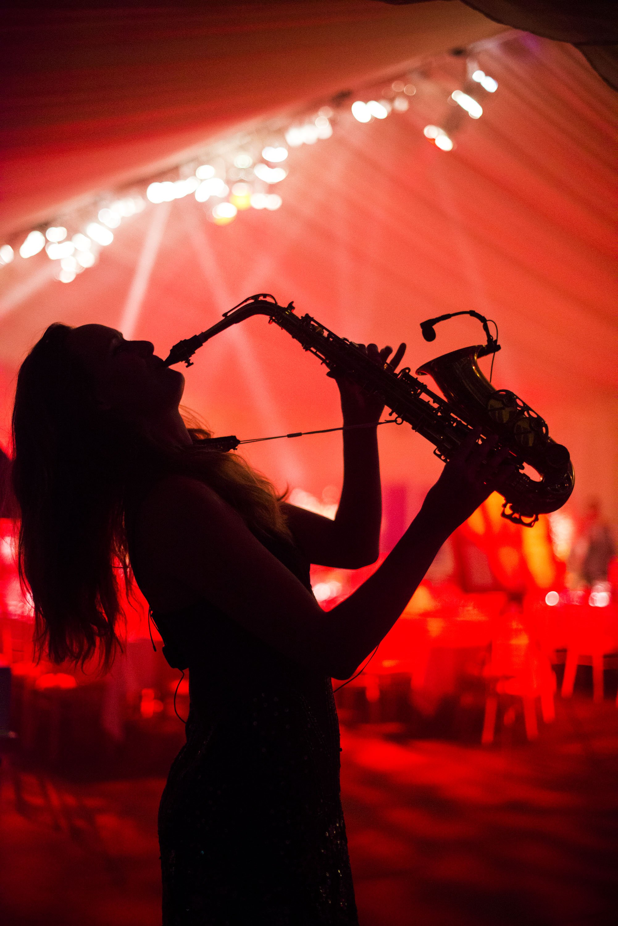 A silhouette of a woman playing a saxophone in a dimly lit setting with red and orange lights.