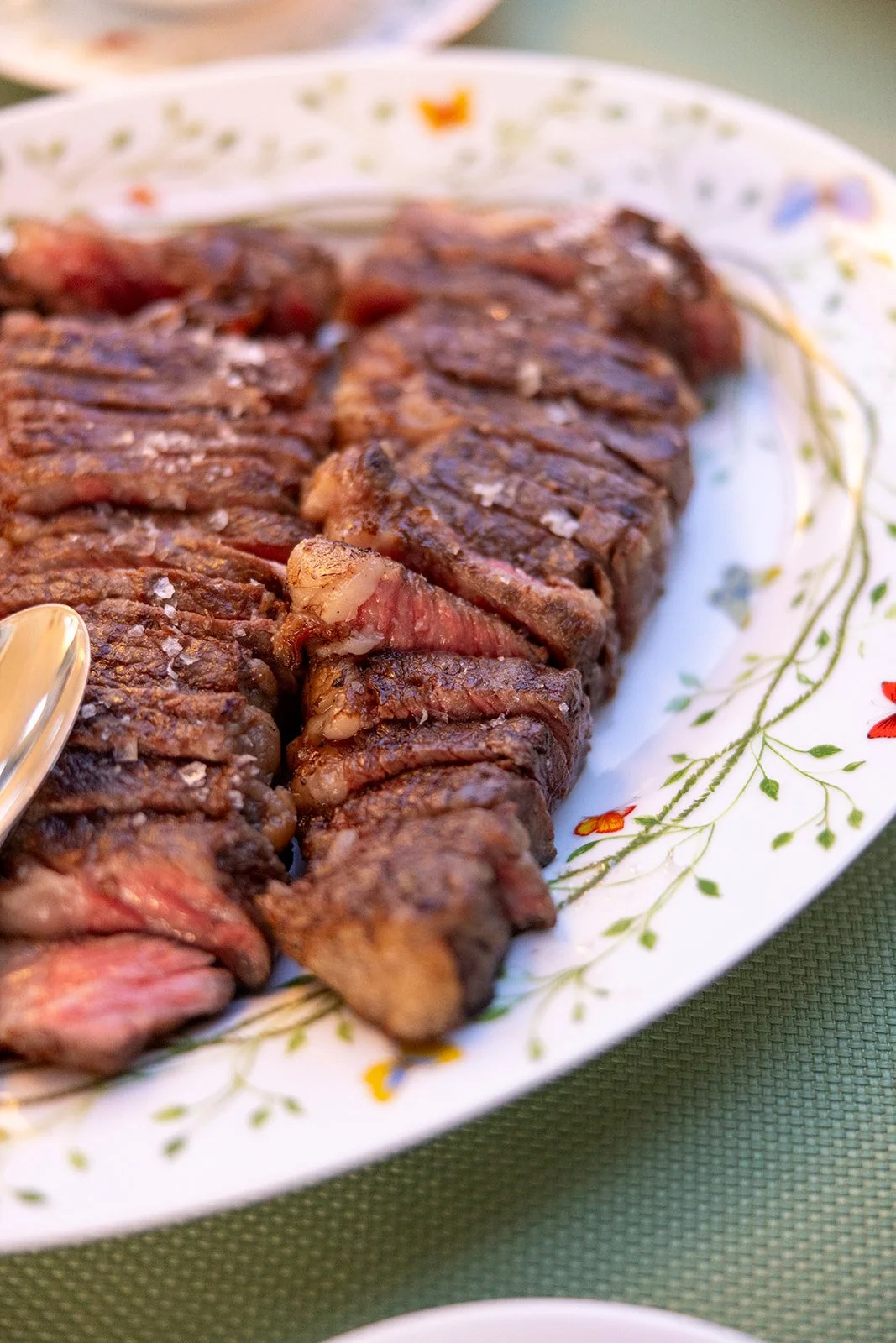Sliced cooked steak on a floral patterned white platter.