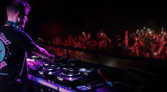 DJ performing at a nightclub with a crowd dancing in the background.