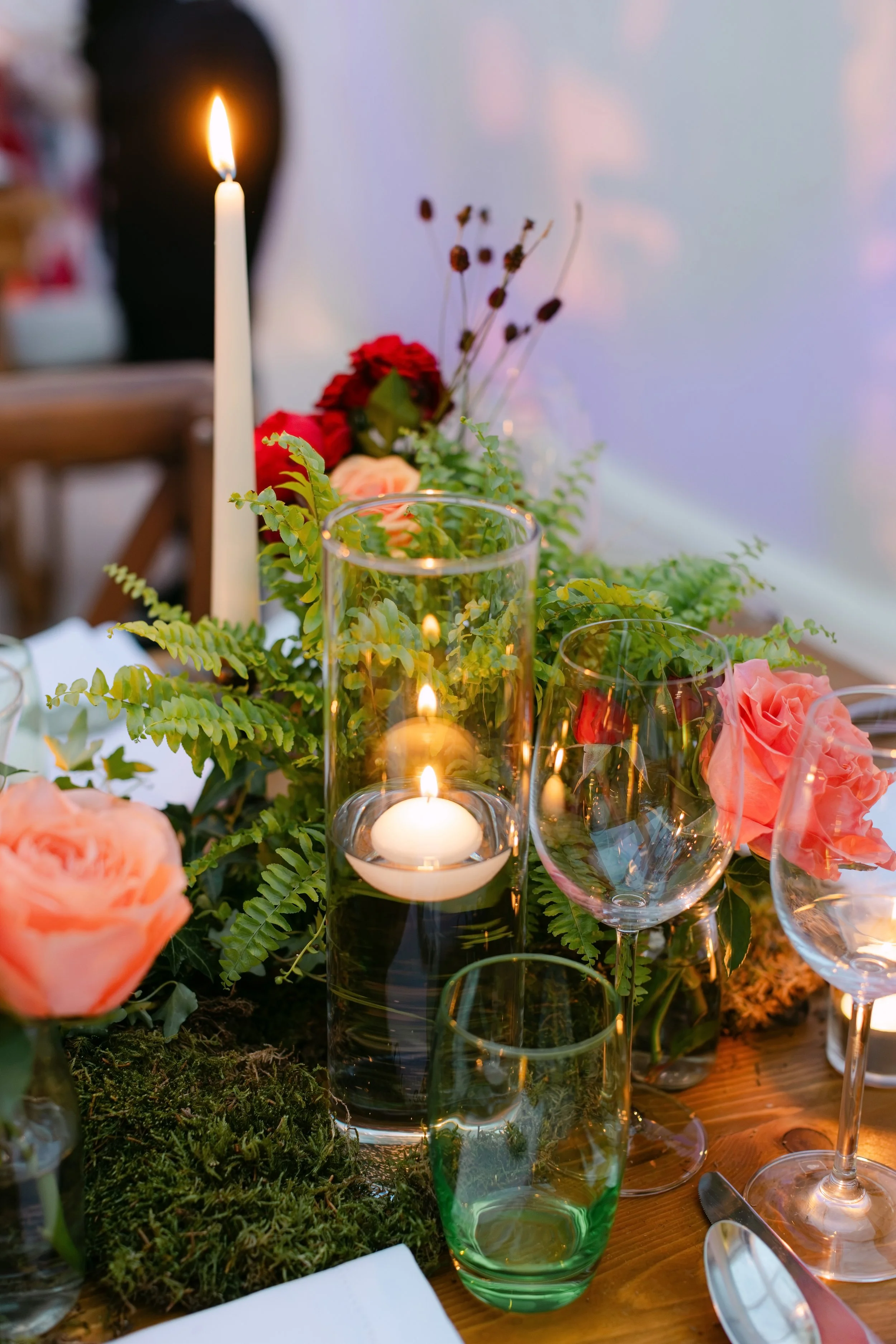 A table decorated with candles, flowers, and greenery, likely for a special occasion or dinner setting.