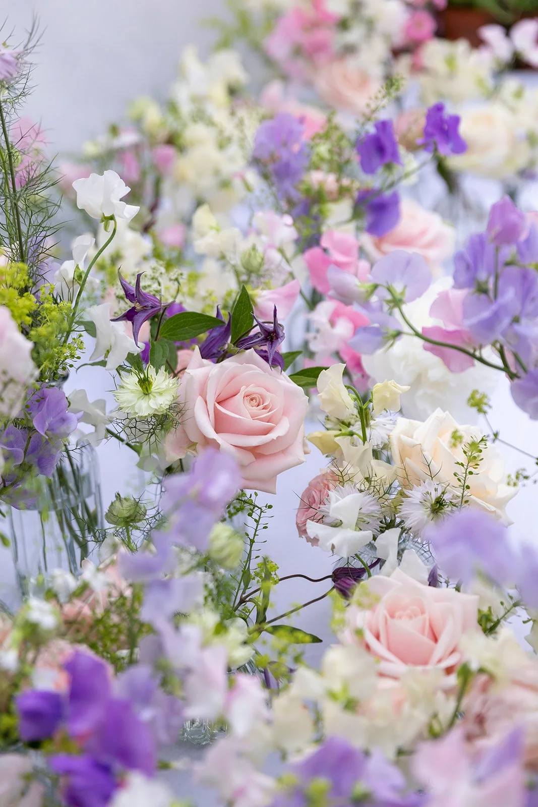 Assorted pastel-colored flowers, including pink roses, purple sweet peas, and white blossoms, arranged in a decorative display.