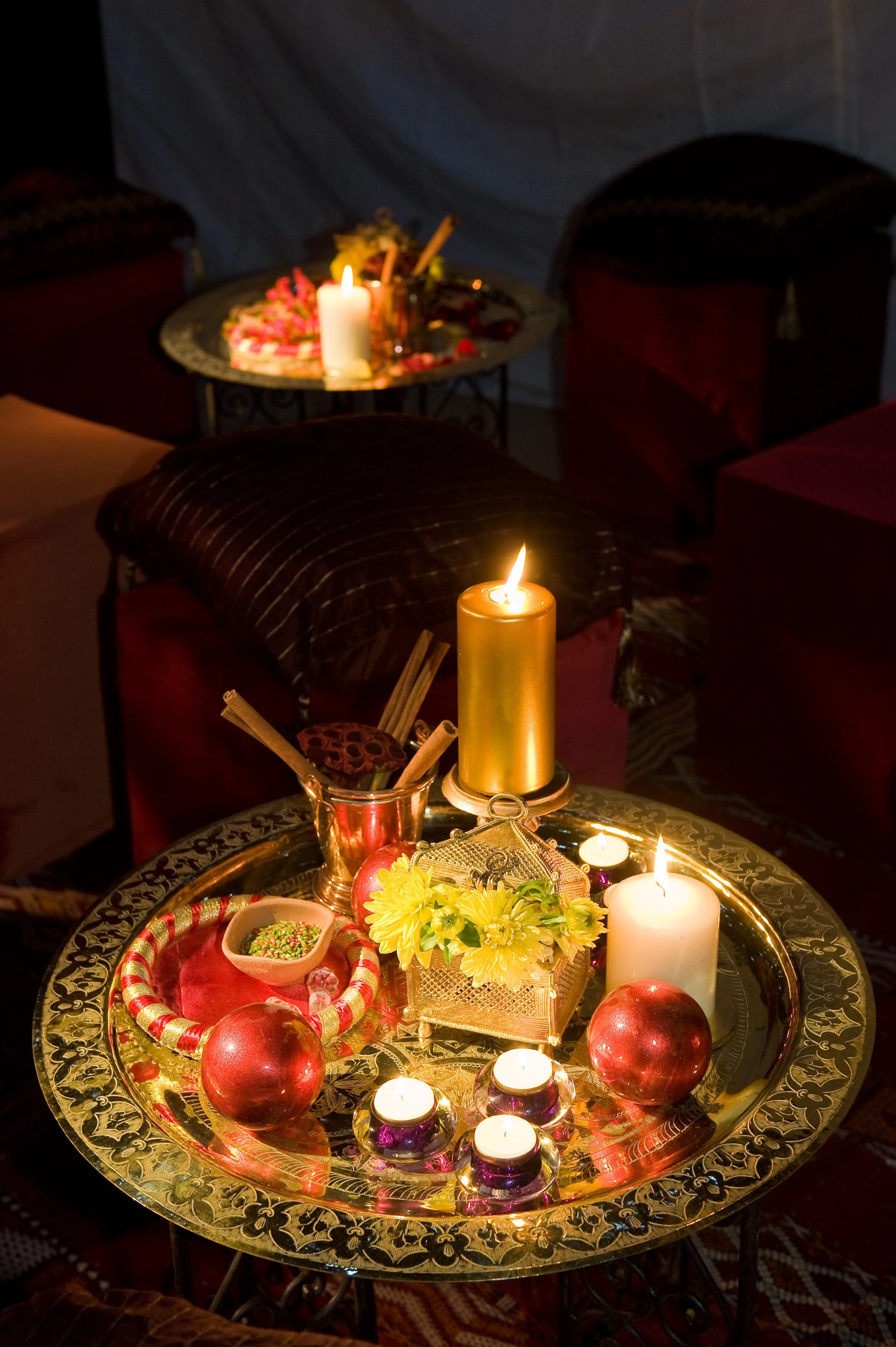 Decorated table with candles, pomegranates, flowers, and small bowls of sweets, surrounded by chairs, in a dimly lit room.