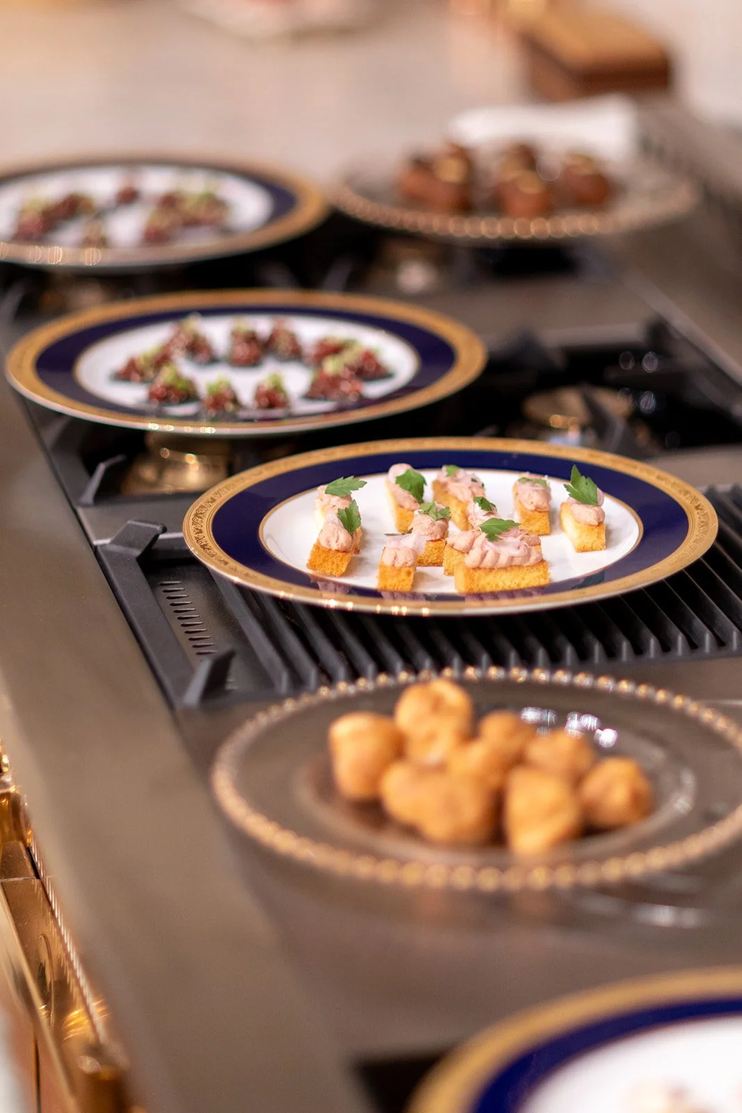 Plates with appetizers, including small crostini topped with pink spread and herbs, on a gas stove.
