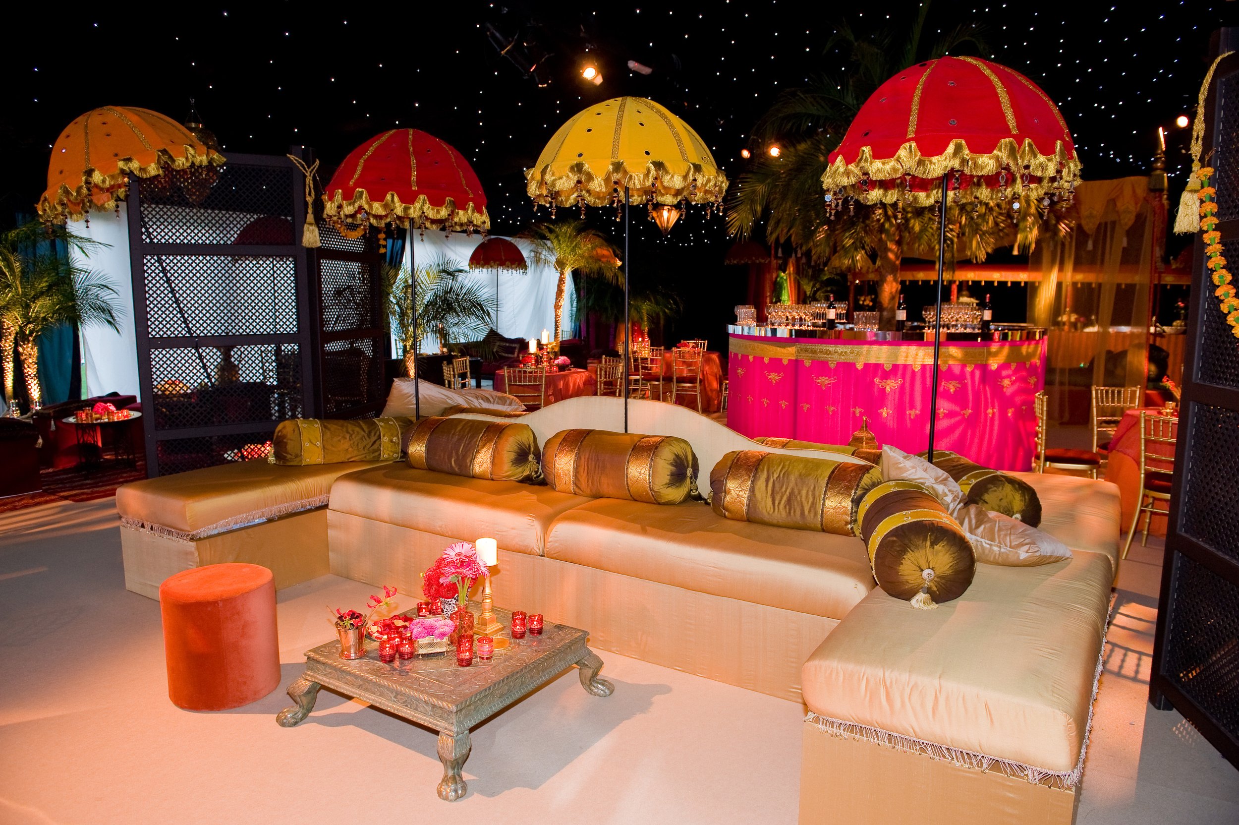 Elegant event space with golden and red umbrellas, plush seating, and floral decor under a starry ceiling.