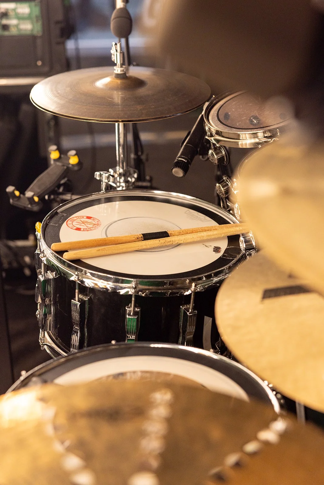 A drum set with a snare drum and drumsticks resting on it, along with a cymbal, in a music studio or performance space.