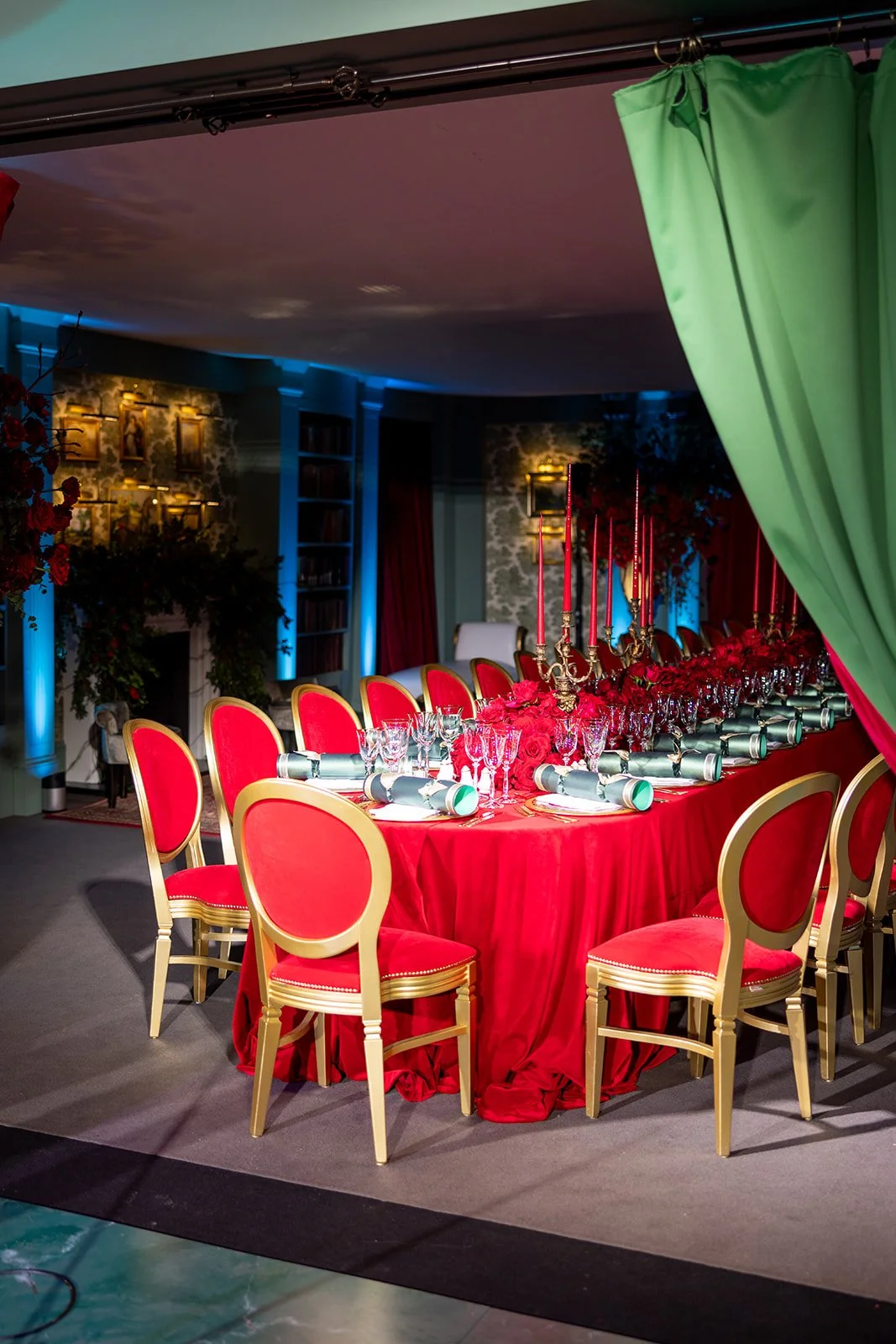 Elegant banquet table setting with red tablecloth, red chairs with gold trim, gold candelabras with red candles, and glassware, decorated for a formal event.