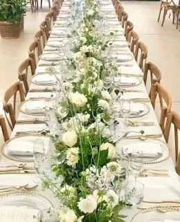 Long banquet table decorated with a white floral centerpiece and elegant table settings for a formal event or wedding reception.