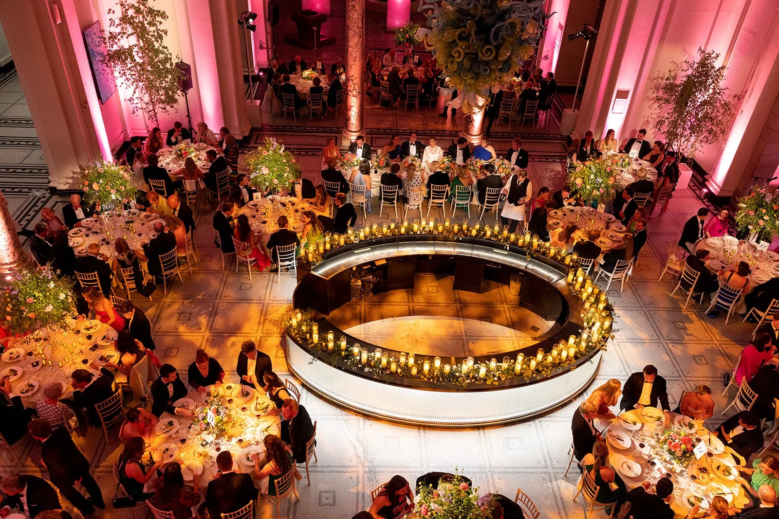 Victoria & Albert Museum Wedding from above showing guests sitting at the tables in low lighting and with elaborate flower arrangements with a central circular bar.
