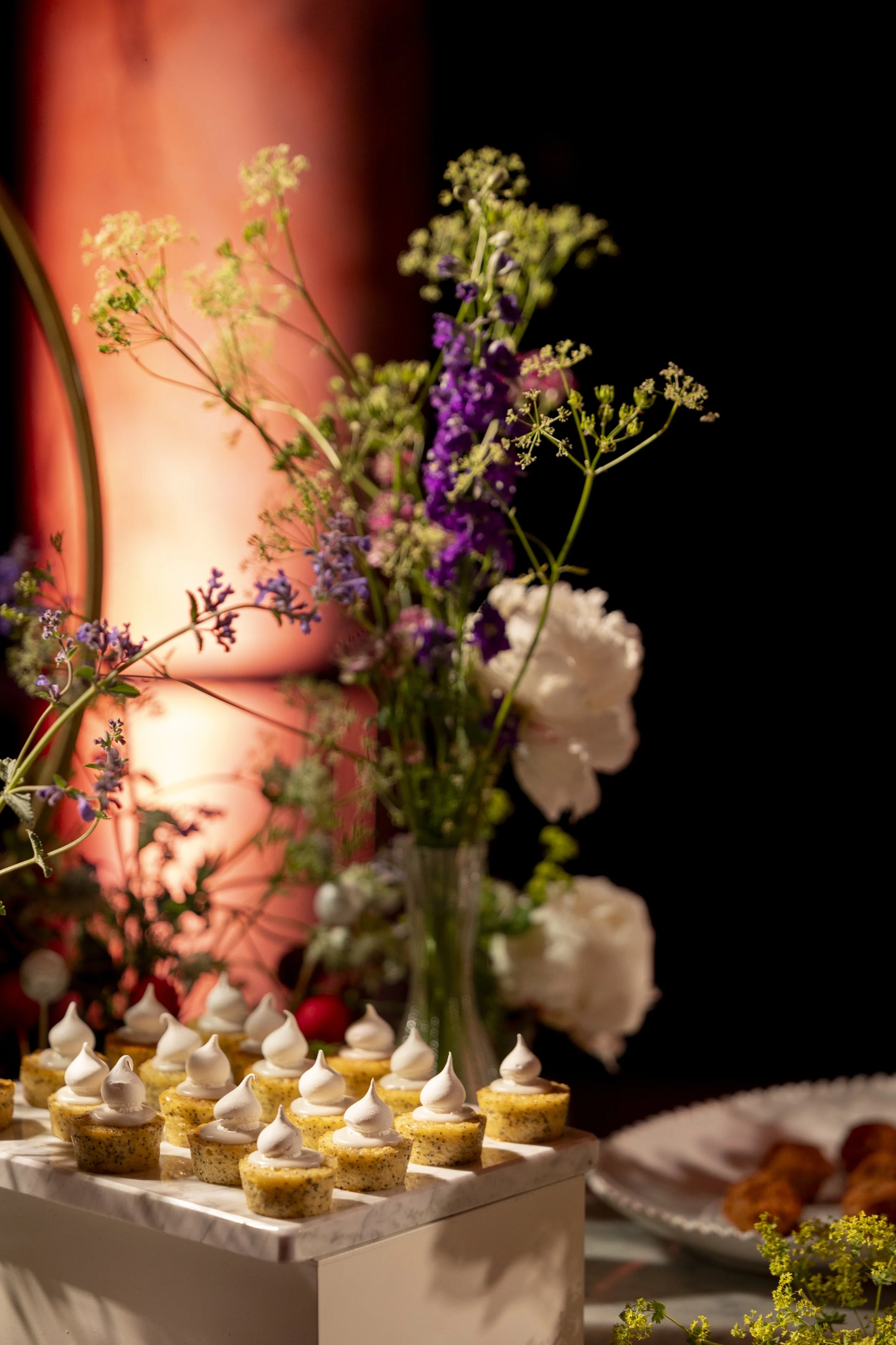 Miniature desserts topped with whipped cream on a marble serving tray with flowers and a cake in the background science a party or celebration.