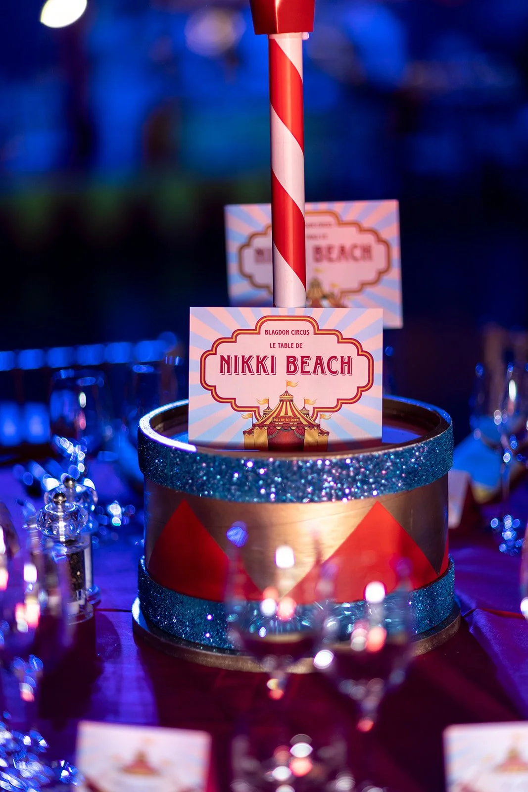 A round circus-themed table number display with a red and gold border, featuring a circus tent illustration and the text 'Nikki Beach' at a party or event.