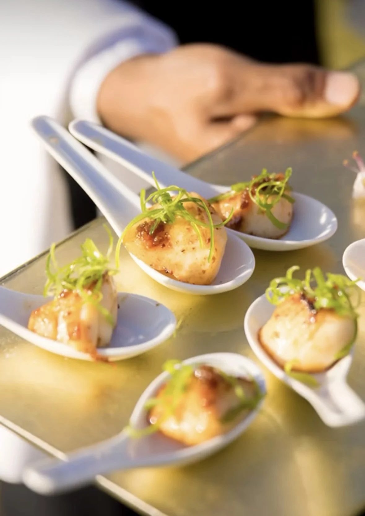 Close-up of bite-sized appetizers served on white ceramic spoons, garnished with green herbs.