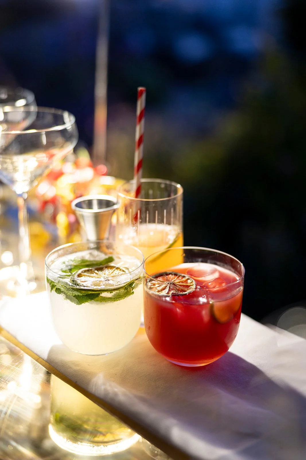 Assorted colorful cocktails with fruit slices and garnishes on a white table at a party or gathering.