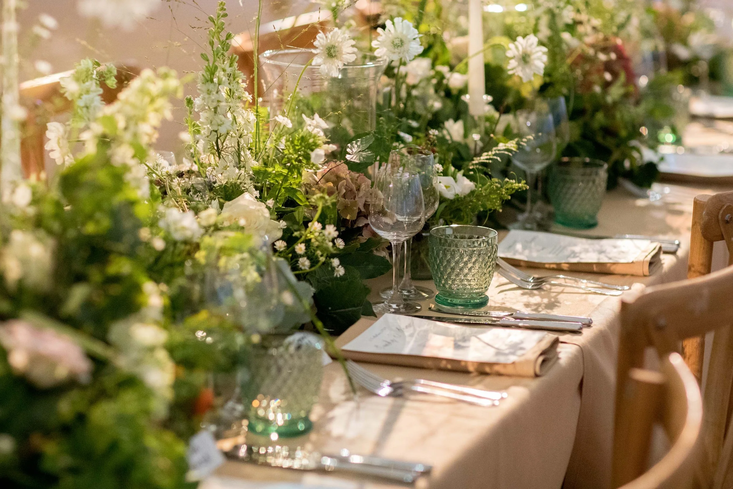 A table decorated with white and green floral arrangements, glassware, and place settings for a formal event or dinner.