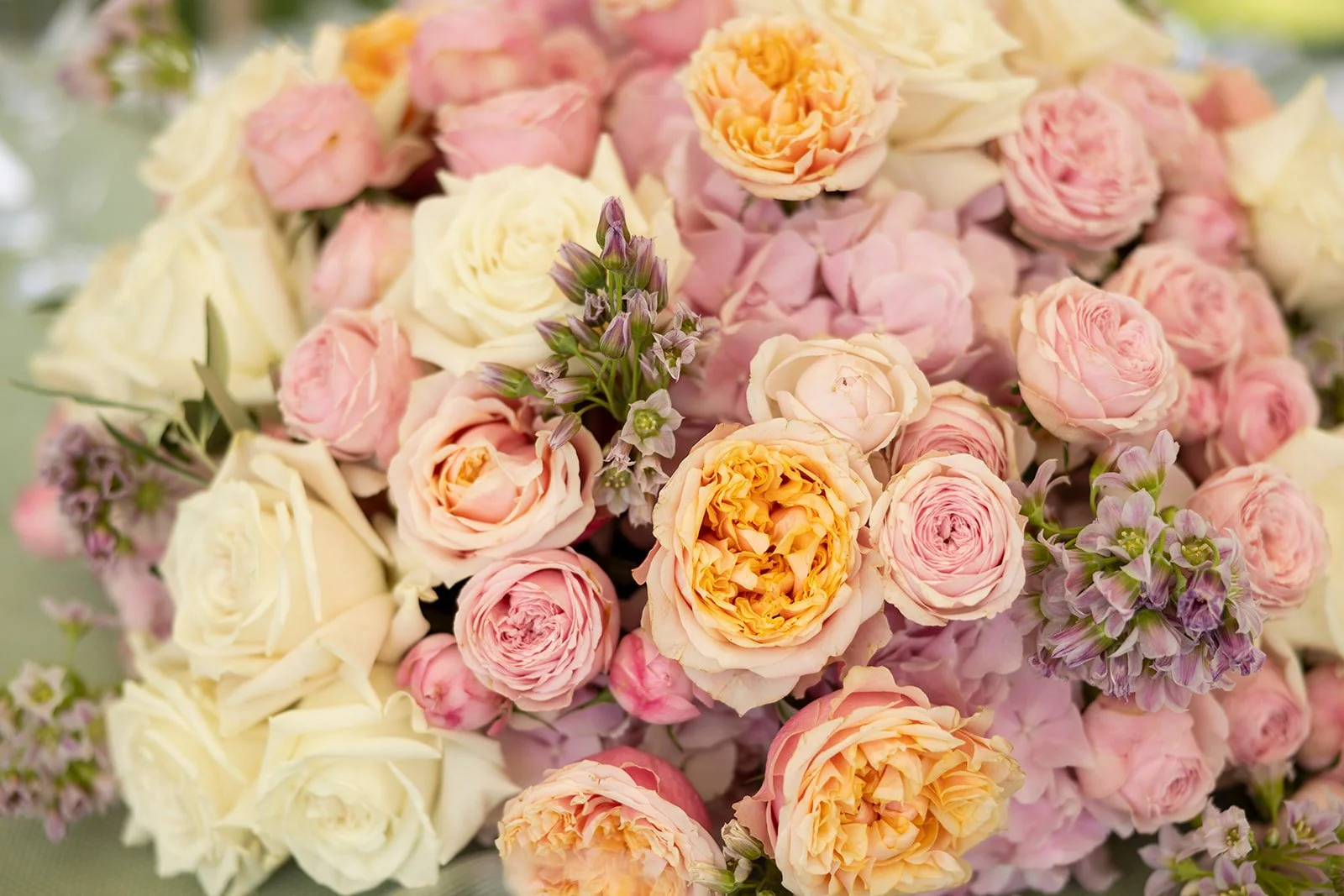 A close-up of a bouquet of roses and other flowers in pastel colors including pink, cream, and peach.