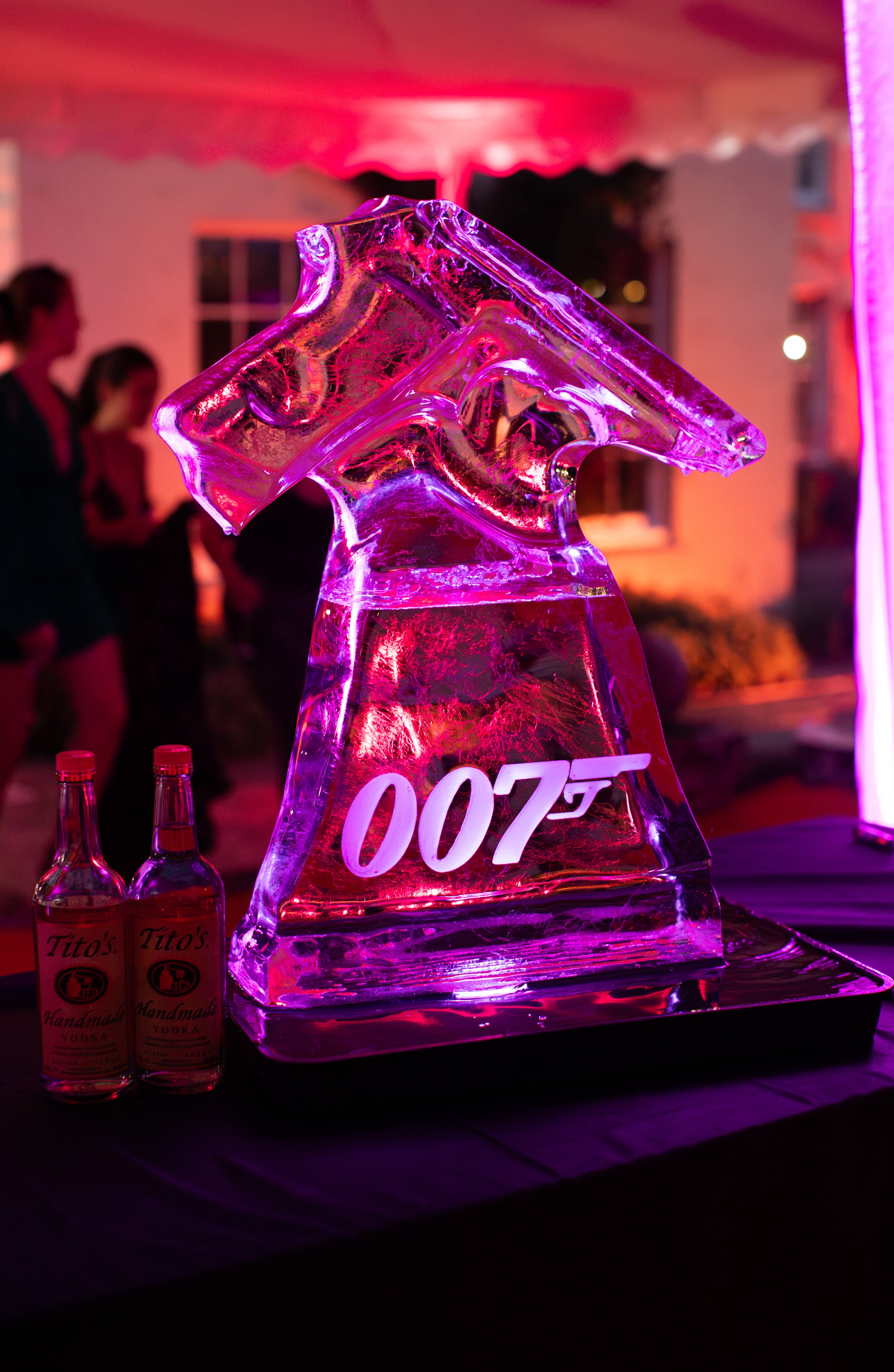 Ice sculpture of the James Bond 007 logo illuminated with pink and purple lighting, with two bottles of Tito's Handmade Vodka in front.
