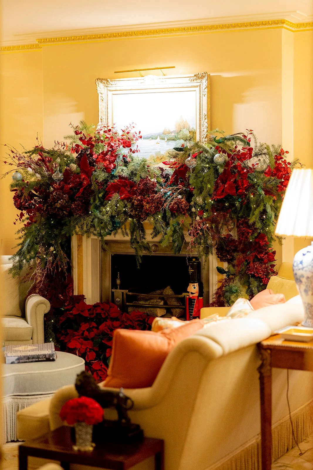 A festive living room decorated for Christmas with a large arrangement of red and green foliage above the fireplace.