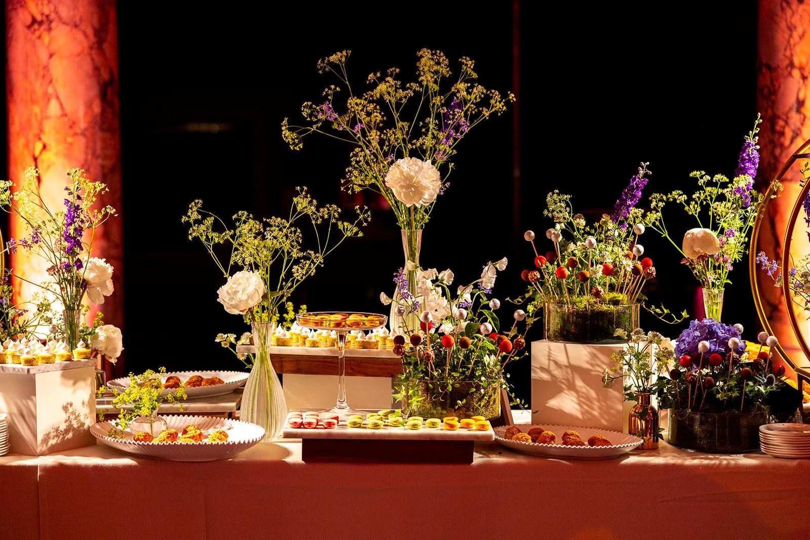 Decorative table display with various flowers in vases and plates of desserts