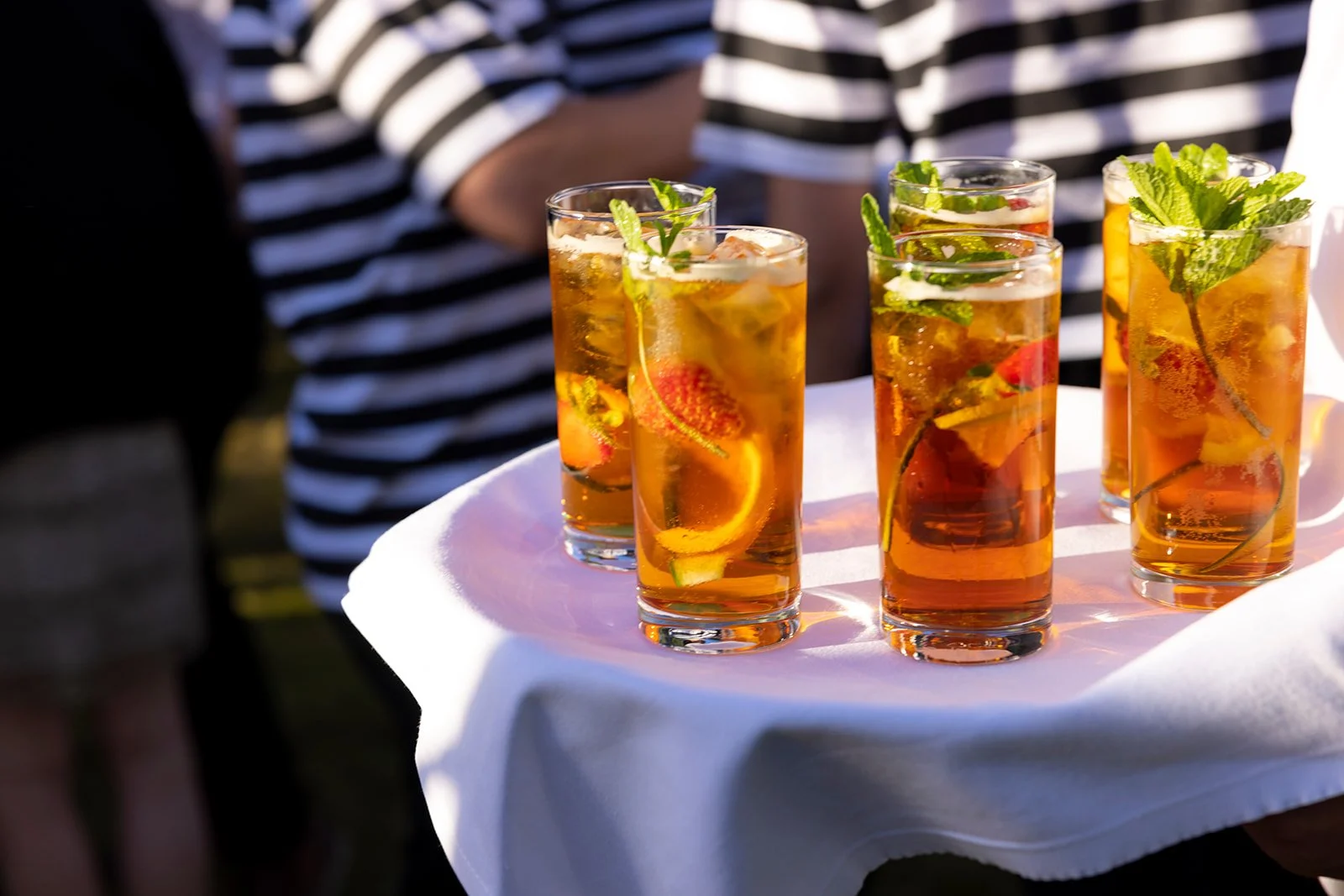 Five tall glasses of iced tea garnished with lemon slices and fresh mint leaves on a white tray.