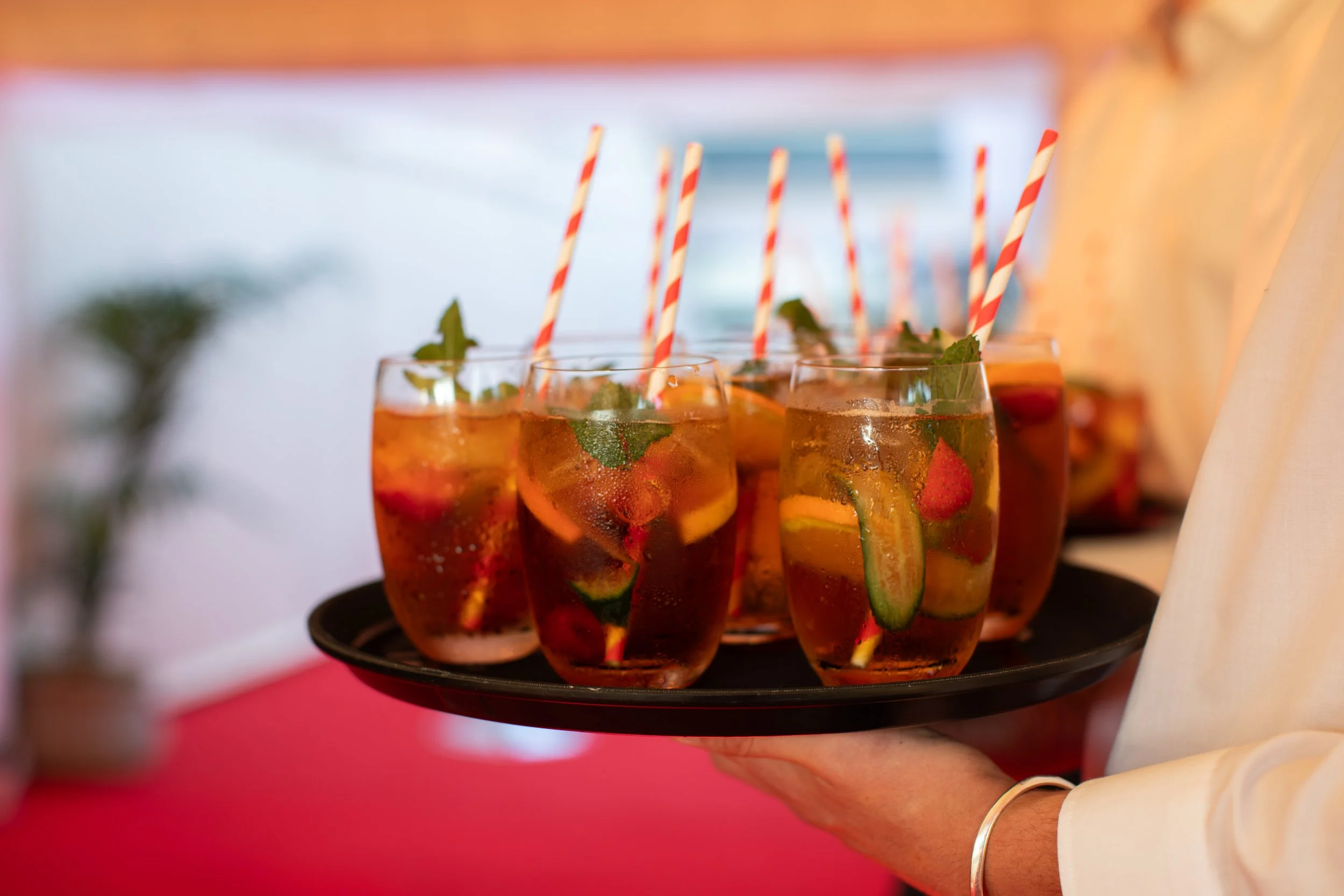 Several glasses of iced tea garnished with mint leaves, lime slices, and strawberries, with red and white striped straws, on a black tray.