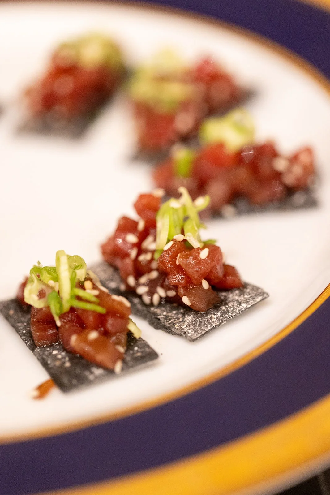 Close-up of spicy tuna tartare bites topped with green onion and sesame seeds, served on black crackers.