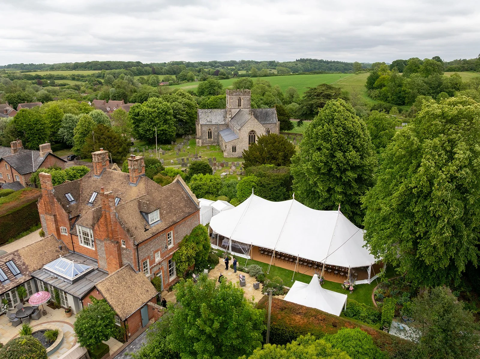 Aerial view of a countryside with old church, residential houses, tents, and lush green trees.
