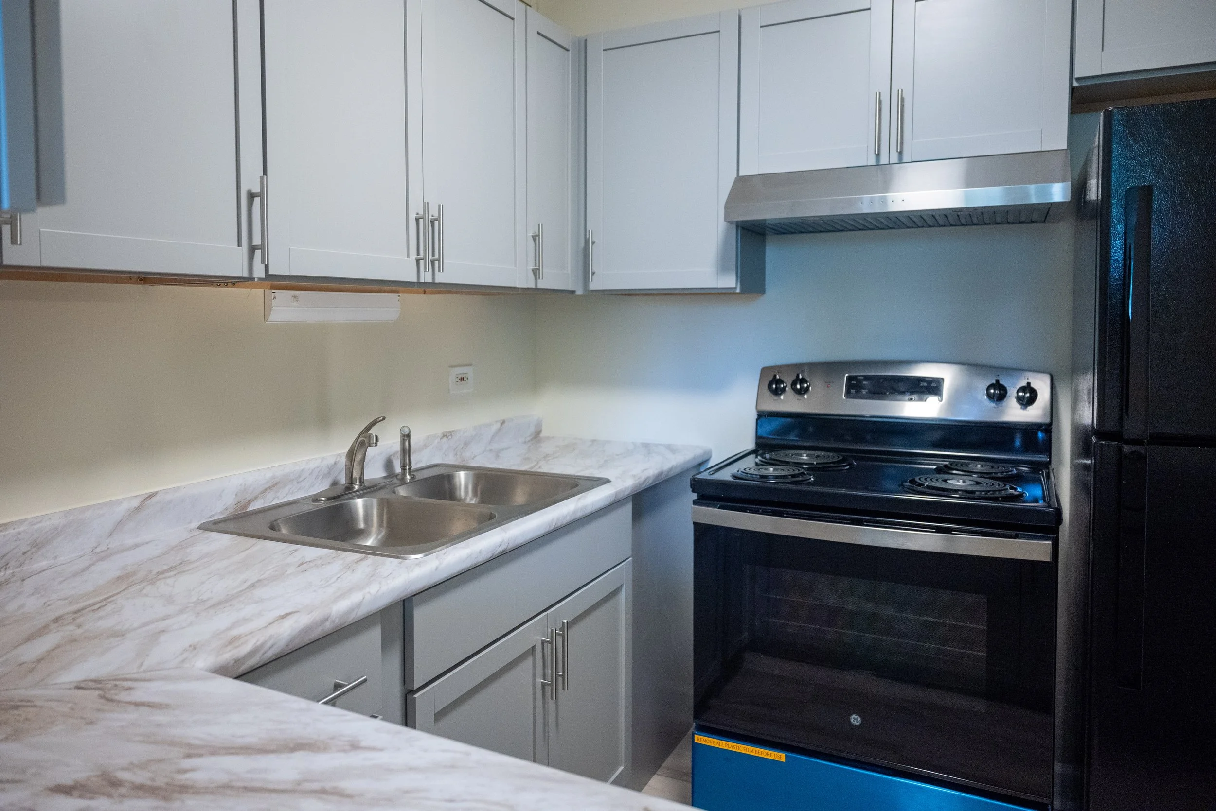 A kitchen with white cabinets, a marble countertop, a double sink, a stainless steel stove, and a black refrigerator.