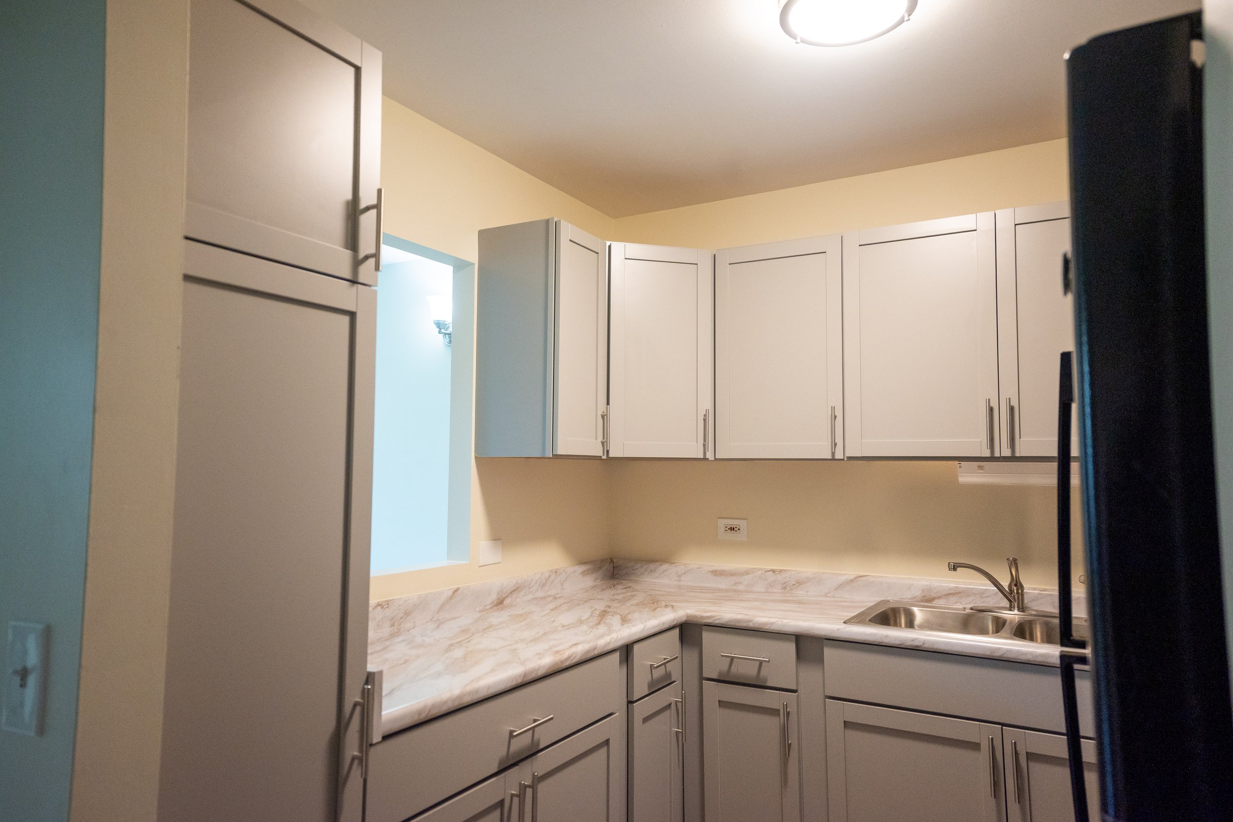 Kitchen with white cabinets, marble countertop, marble backsplash, stainless steel sink, and a ceiling light fixture.