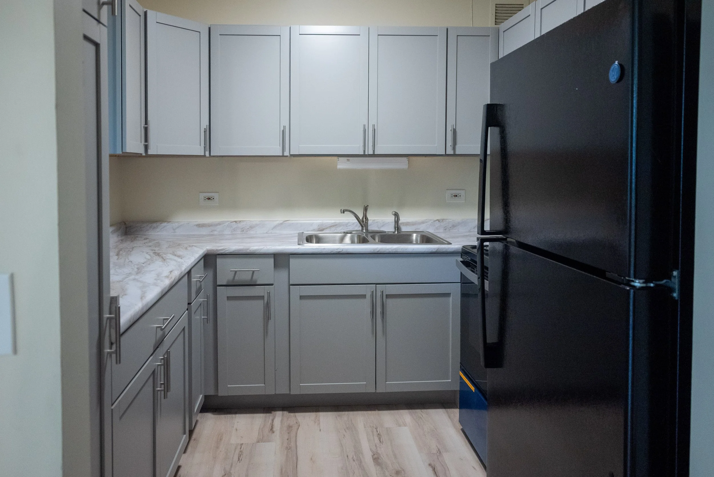 Modern kitchen with gray cabinets, a marble countertop, a double sink, and a black refrigerator.