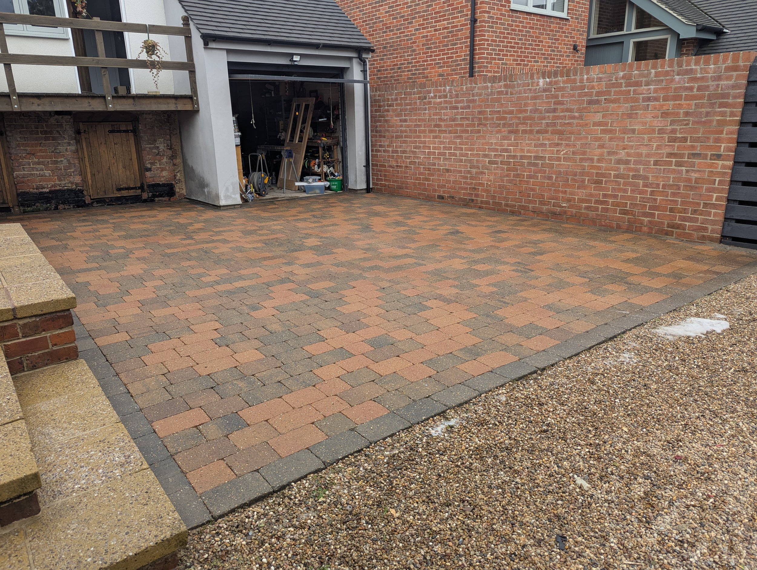 A paved backyard with a color pattern of red, gray, and brown bricks. This Driveway has just been pressure washed by Jet Set Wash - Exterior Cleaning. Now ready for a Re-Sand