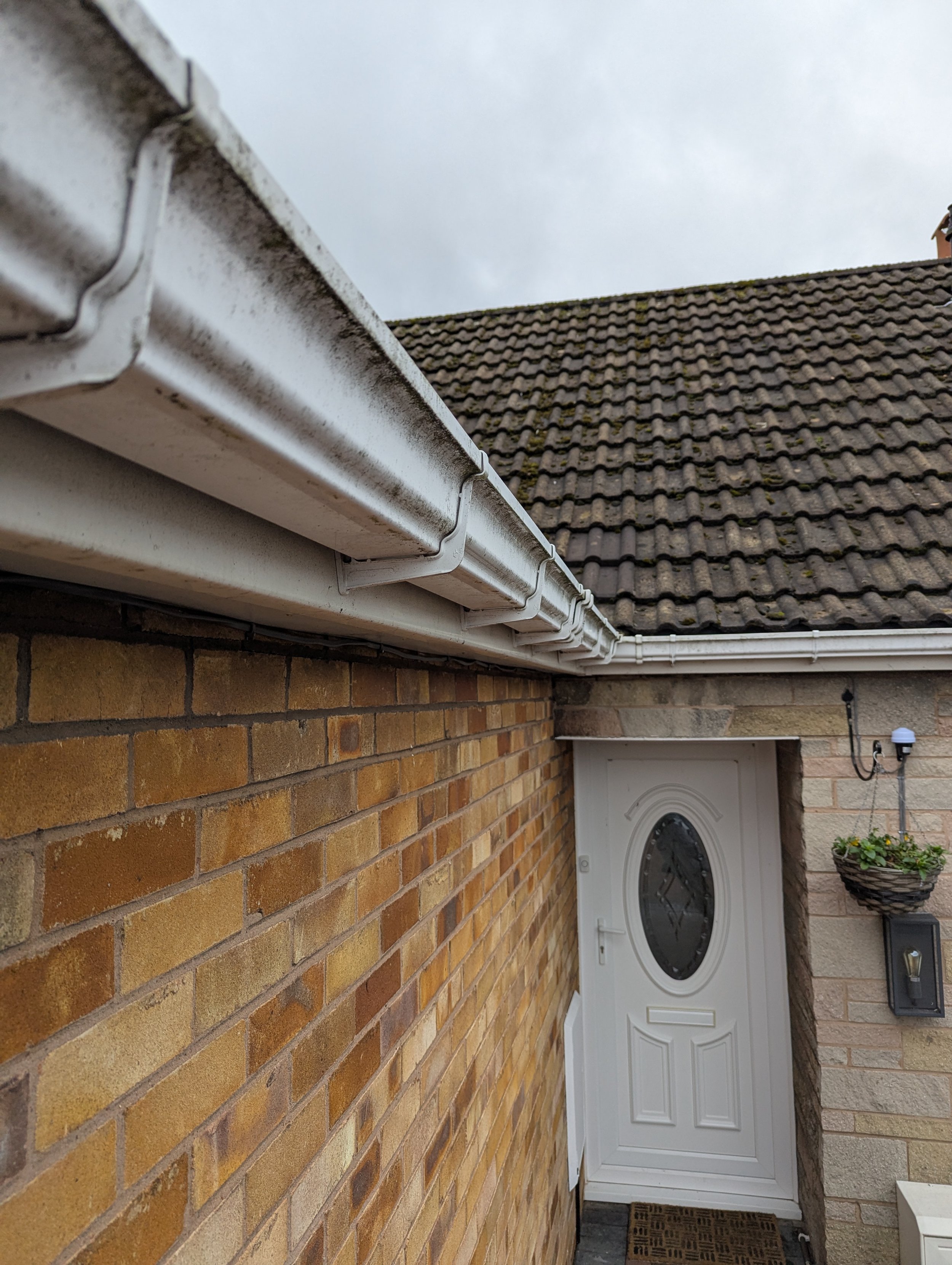 Close-up of the house's white gutter and downspout system against a brick wall and front door with hanging flower basket.
