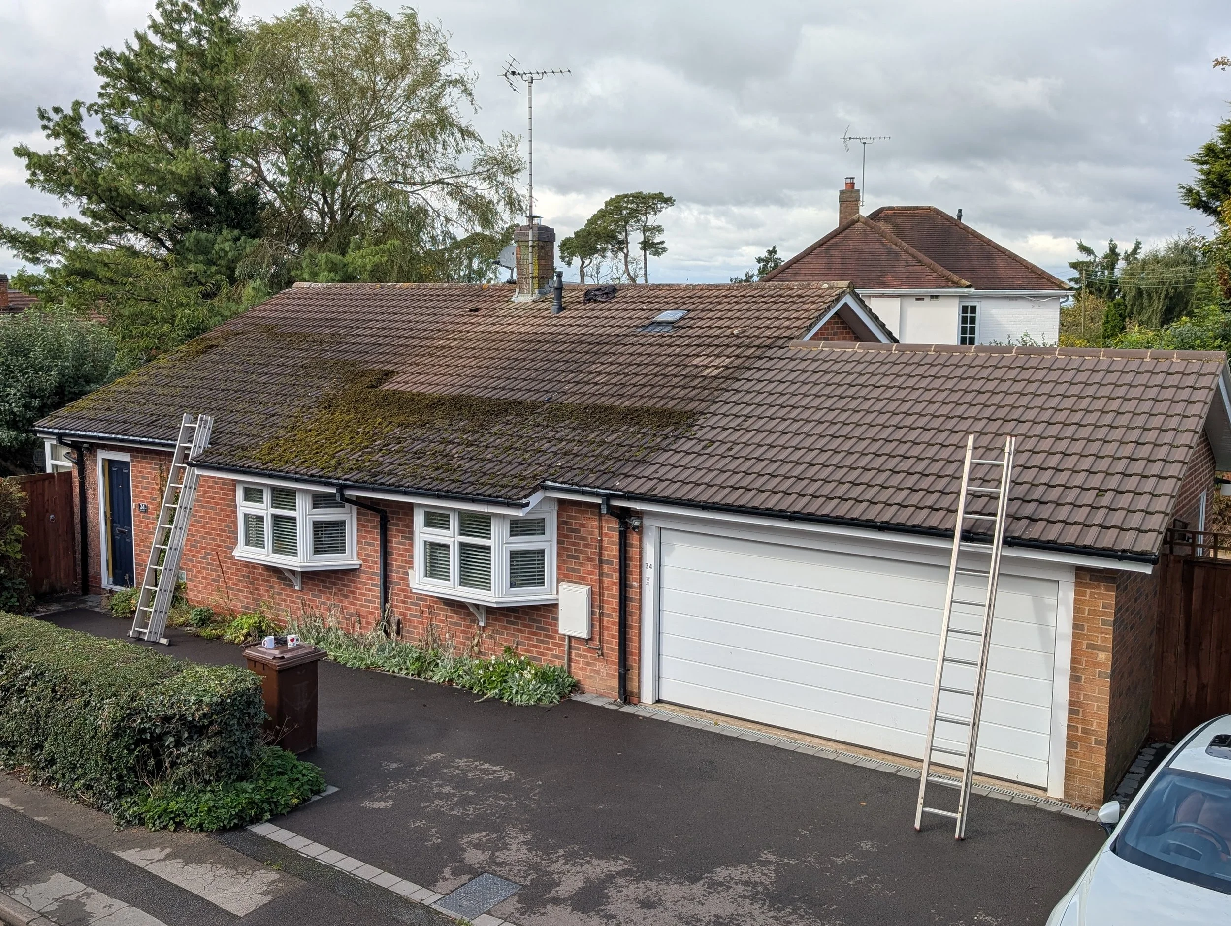 A house with a partially scraped roof, and partially clean roof. The dirty side is full of moss and algae, and the clean side is ready to be chemically treated