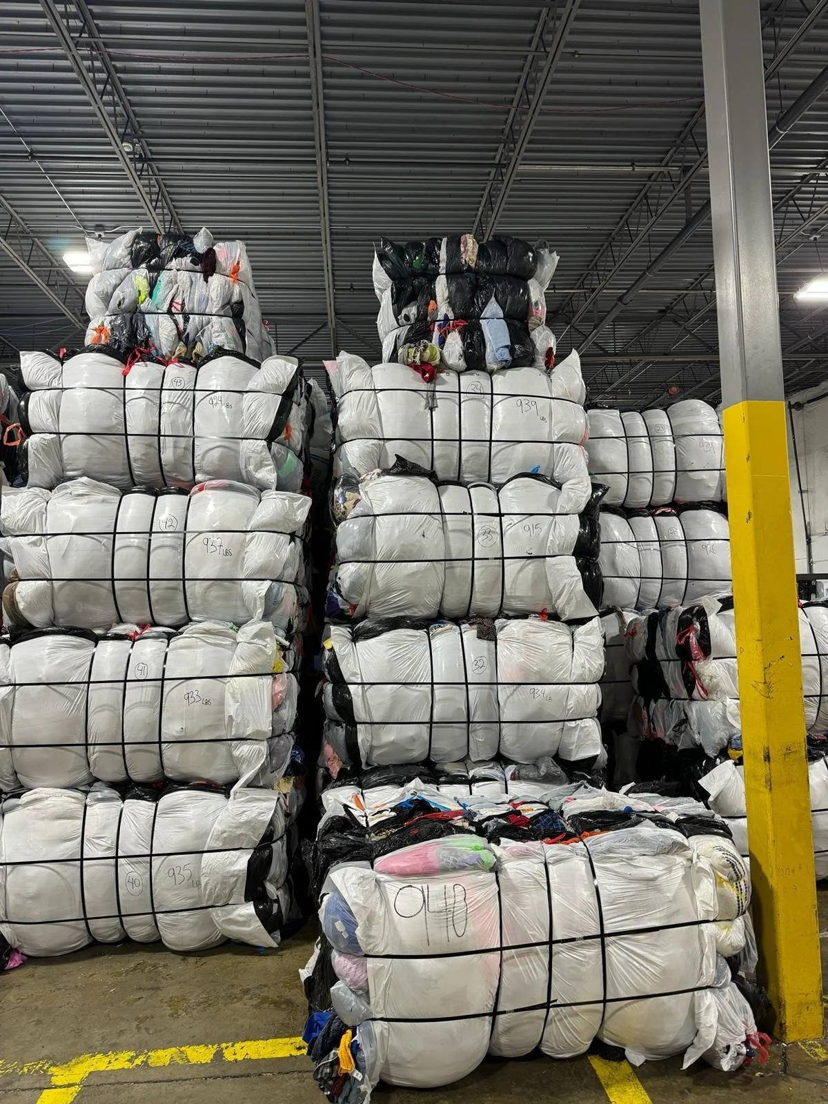 Large stacks of clothing bales containing collected clothing in a warehouse.