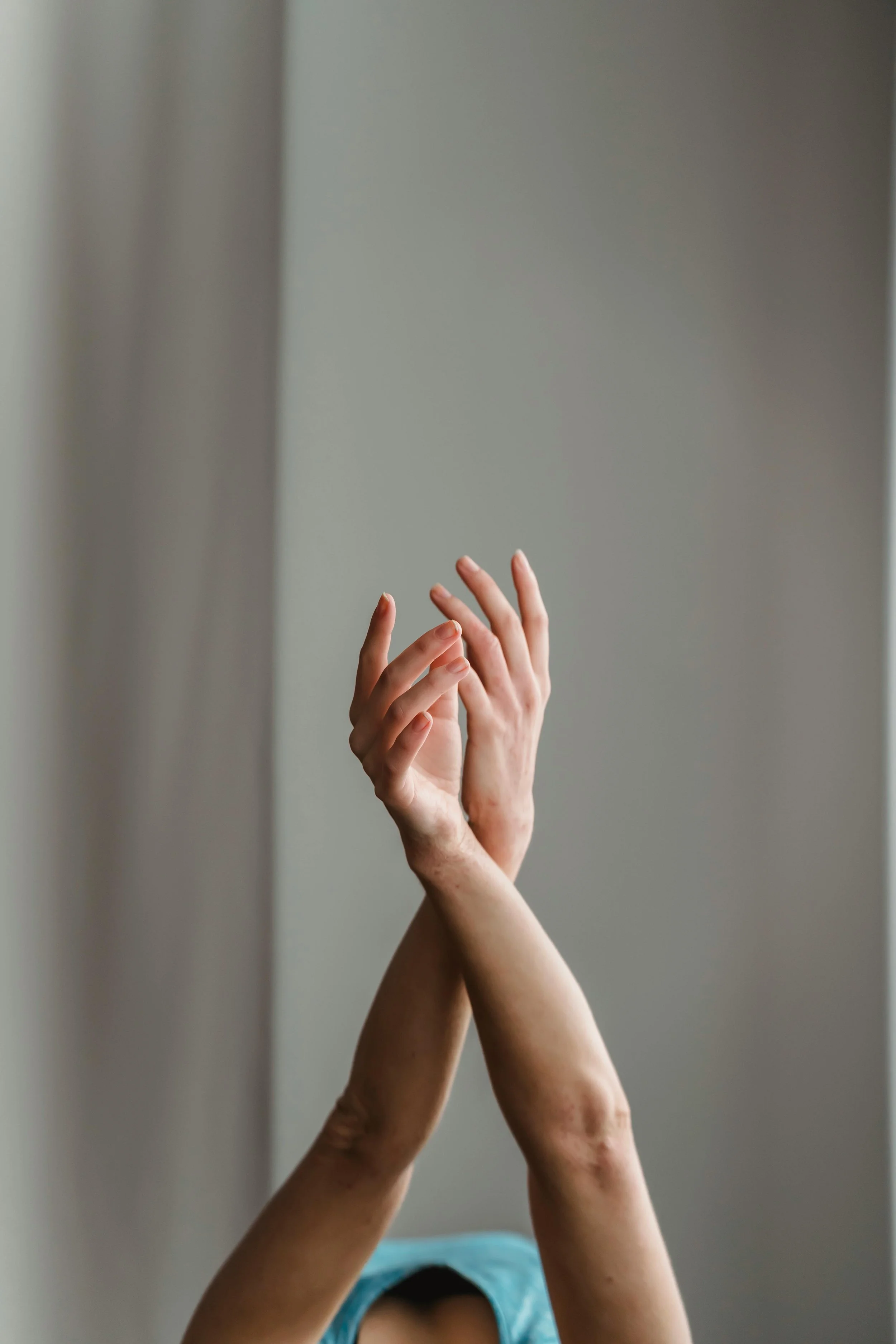 A person with long dark hair, wearing a blue shirt, is taking a selfie in front of a mirror. The image mainly shows multiple hands, including their own, reaching up toward the mirror. The background appears to be a plain wall.