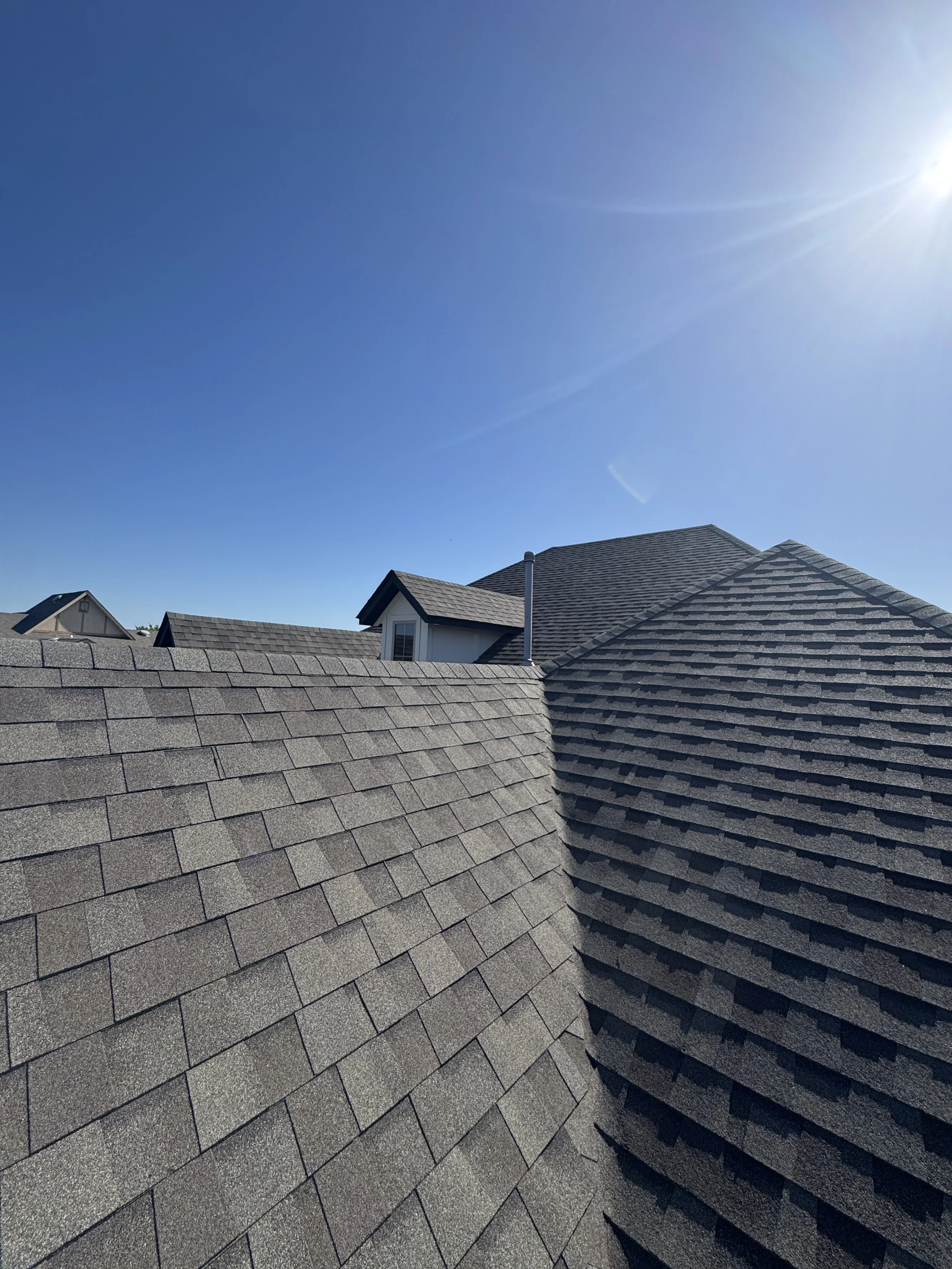 View of multiple rooftops with brown asphalt shingles under a clear blue sky with bright sunlight
