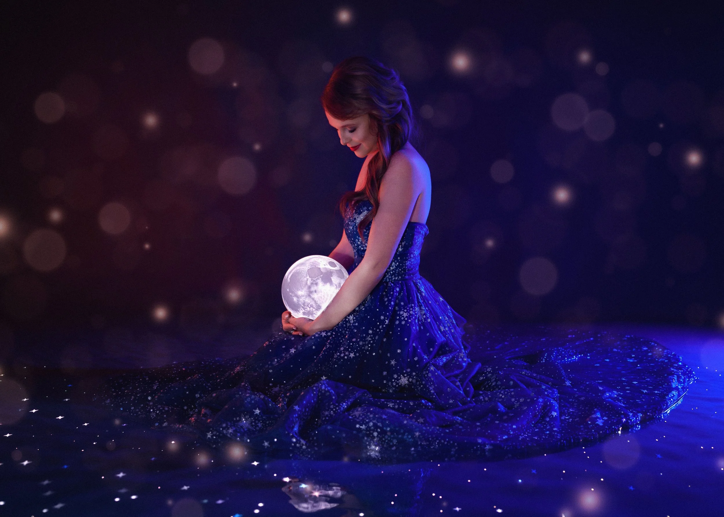 A woman in a starry blue dress sitting on a reflective surface, holding a glowing moon lamp, with a background of dark space filled with glowing orbs and star-like specks.