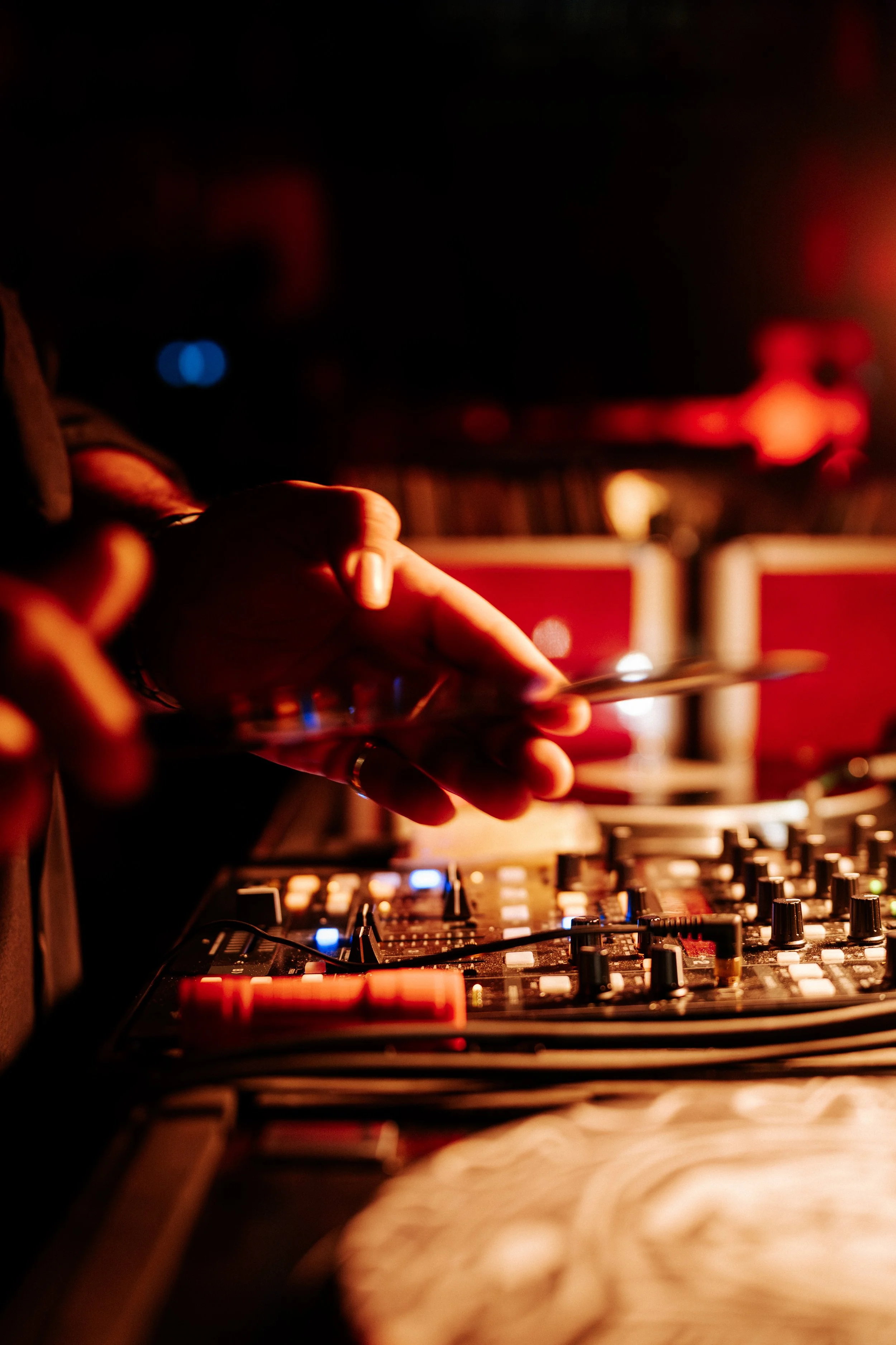 Close-up of a DJ's hand adjusting controls on a mixing console with red and blue lights, blurred background, in a dark setting.