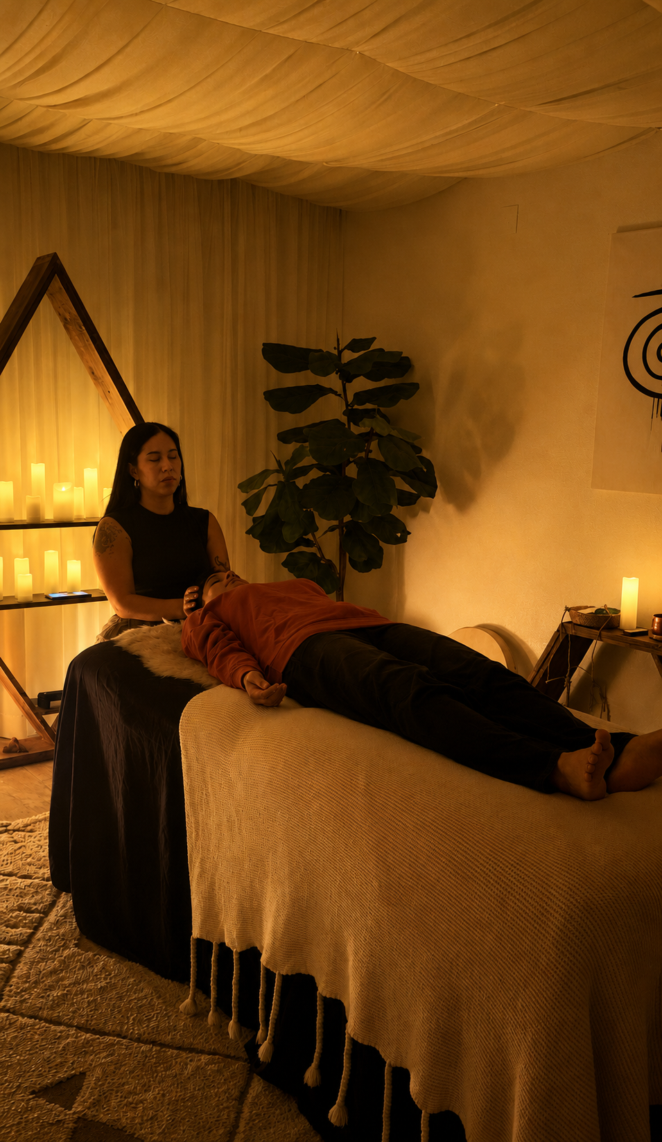 A woman receiving a massage in a dimly lit room decorated with candles, a large plant, and minimalist artwork.