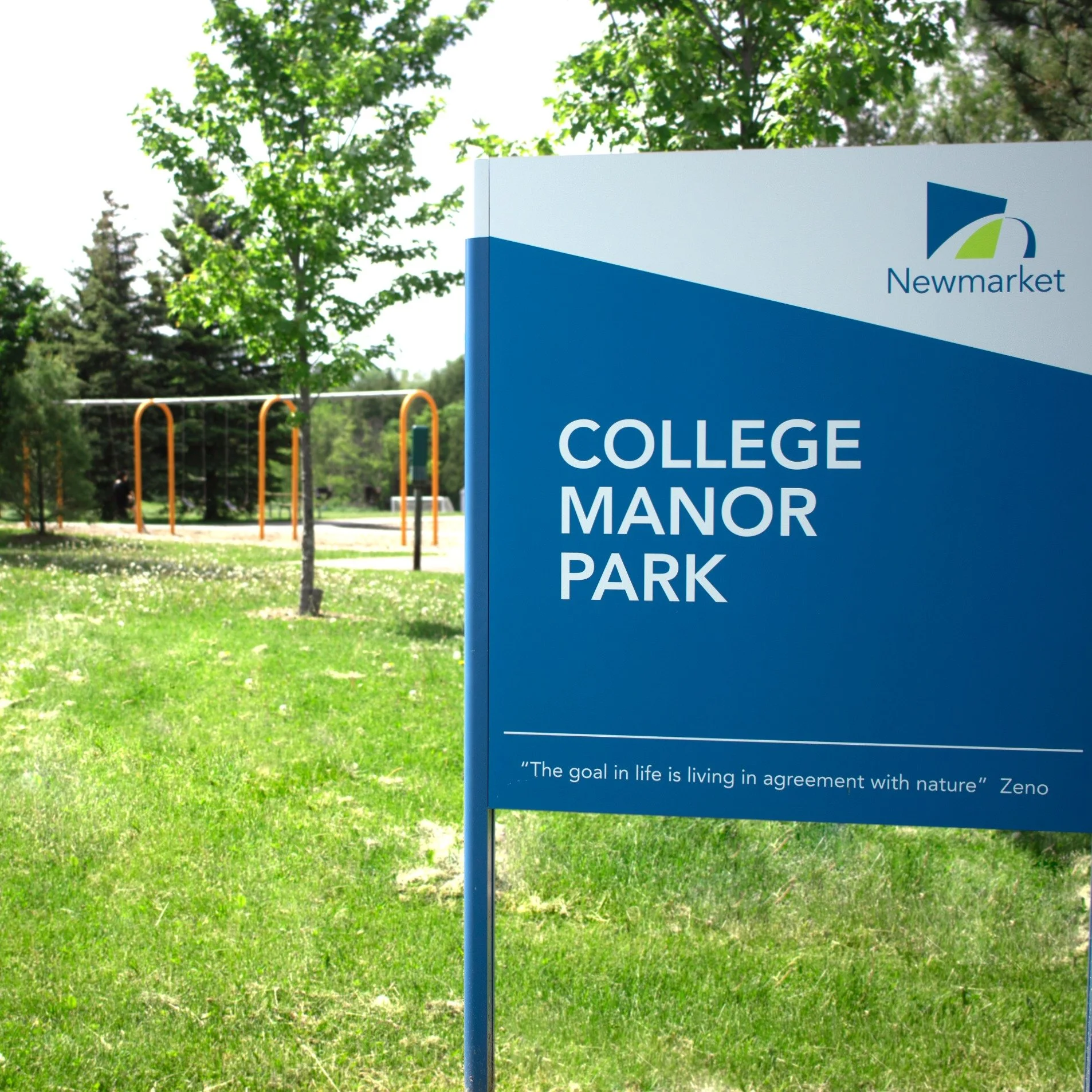 A view of the College Manor Park sign with the playpark in the background.