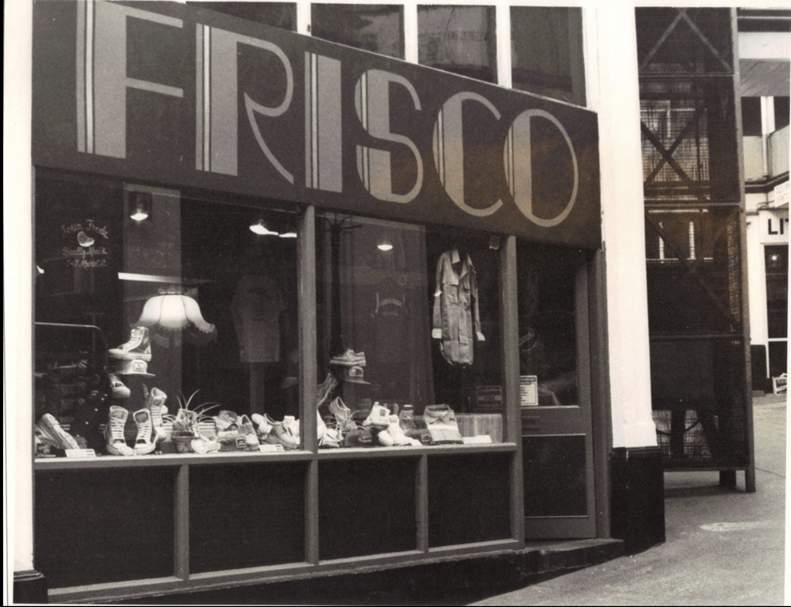 Storefront with shoes and clothing inside, large sign with partially visible letters 'FRISCO' above the window. Outside of Frisco in the Handyside Arcade