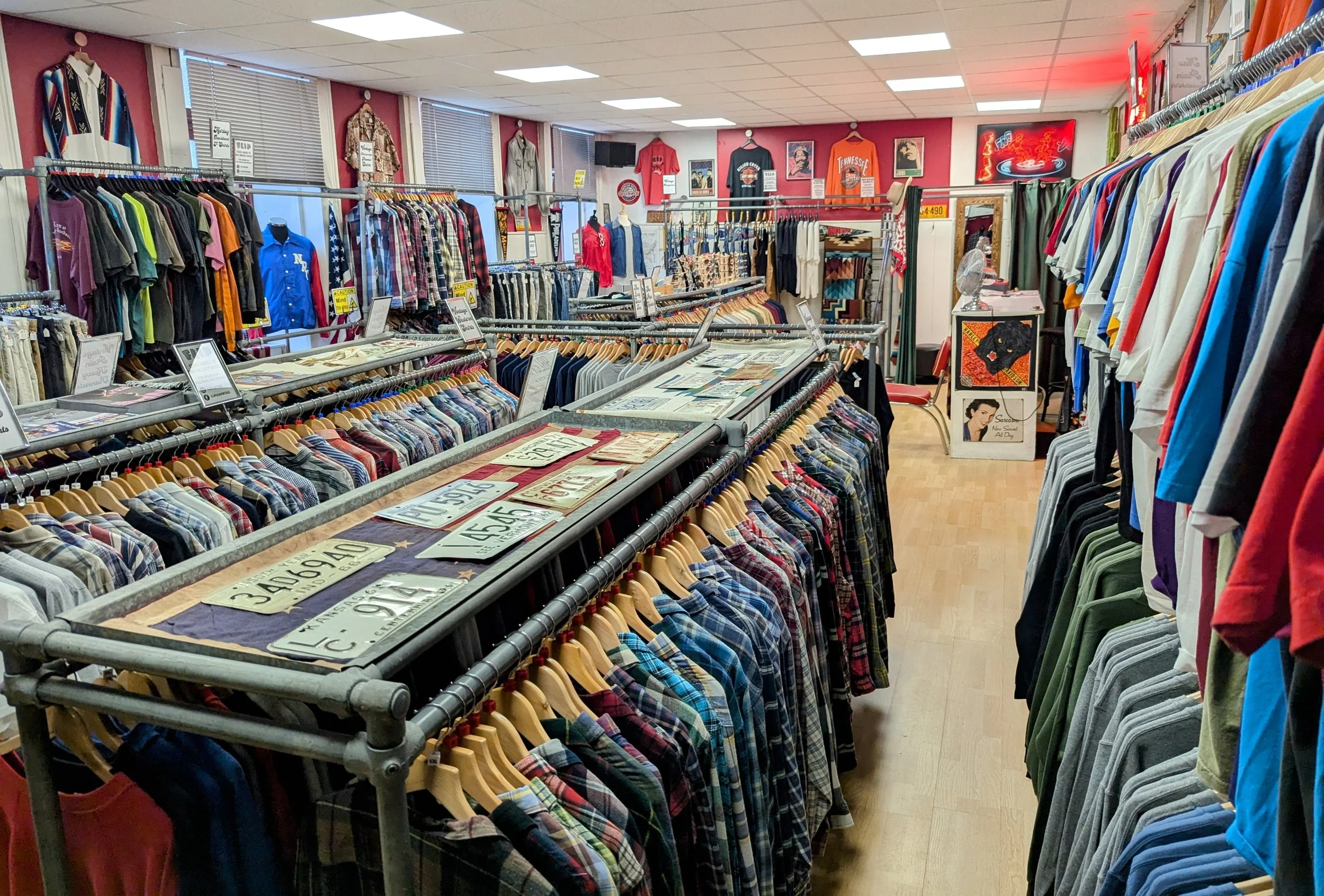 Interior of Flip vintage shop with racks of clothing, including plaid shirts, t-shirts, and jackets. The walls are decorated with posters and memorabilia, and there are signs and price tags on the racks.