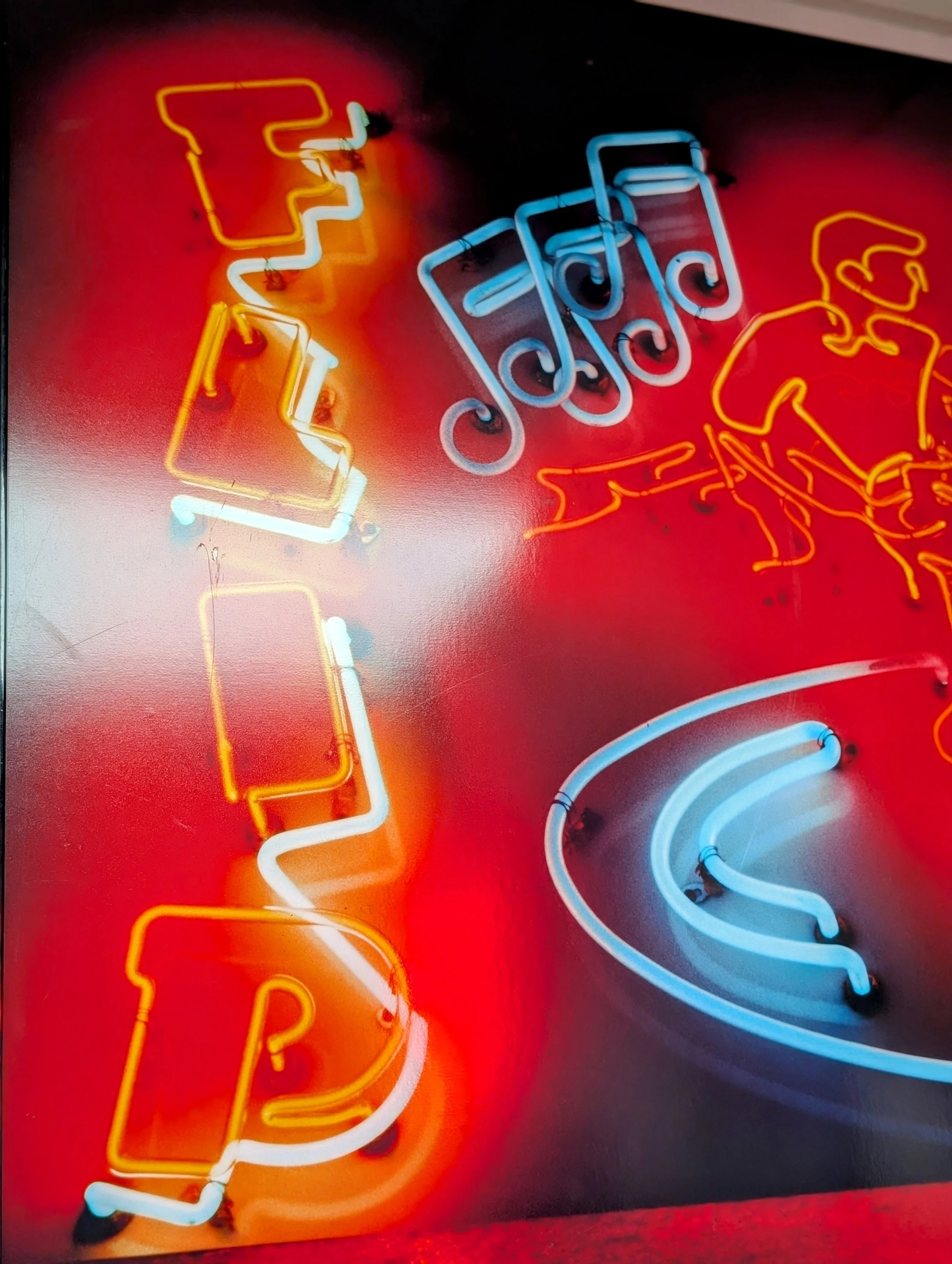 Colorful neon sign with yellow and white text, and blue spiral design, illuminated against a red background.
