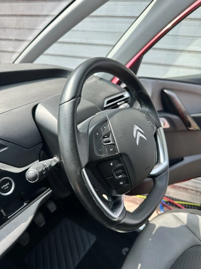 Close-up of a Citroën car steering wheel with buttons, a dashboard, and start button visible inside the vehicle.