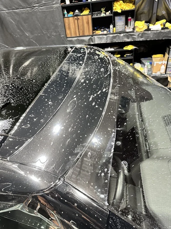 Close-up of a black car with soap suds on the windshield in a garage or workshop setting.