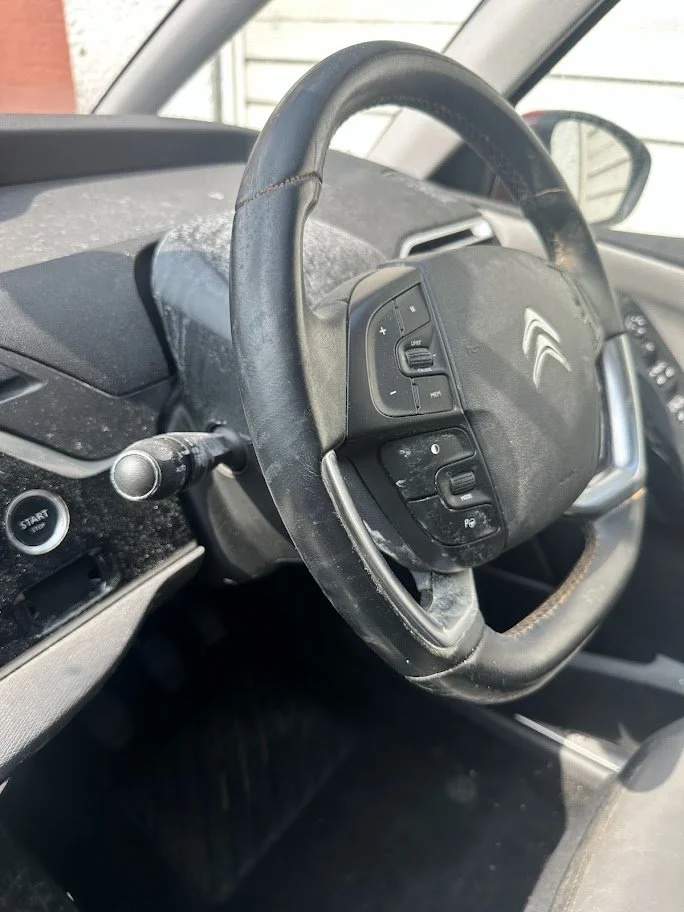 The image shows the interior of a Citroën vehicle, focusing on the steering wheel, which has mounted controls, and the dashboard with a dust or dirt accumulation.